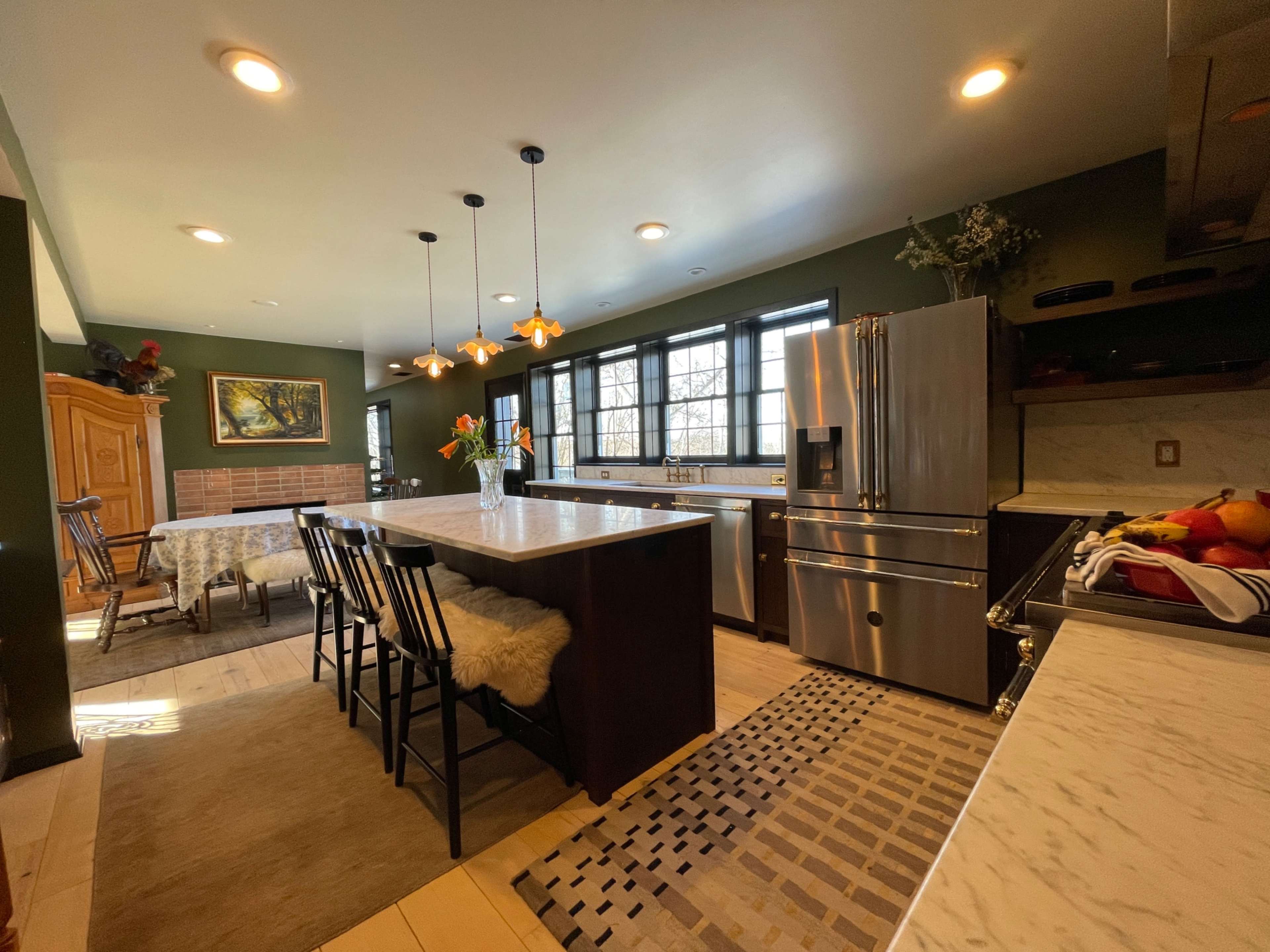 The kitchen features a central island with seating, modern appliances, and large windows allowing natural light to enter.