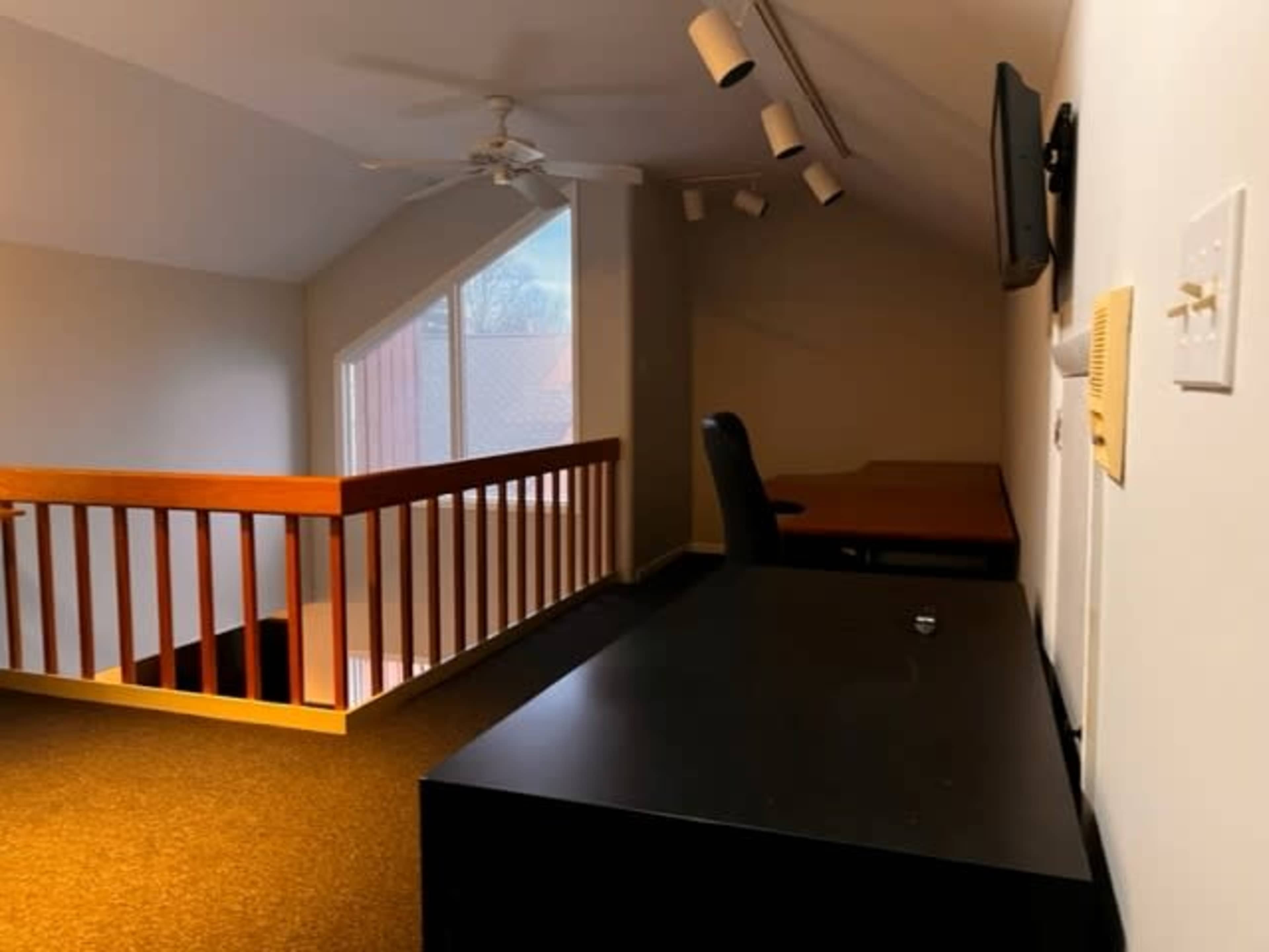 A lofted space featuring a desk, a chair, a television, and a railing overlooking a lower level.
