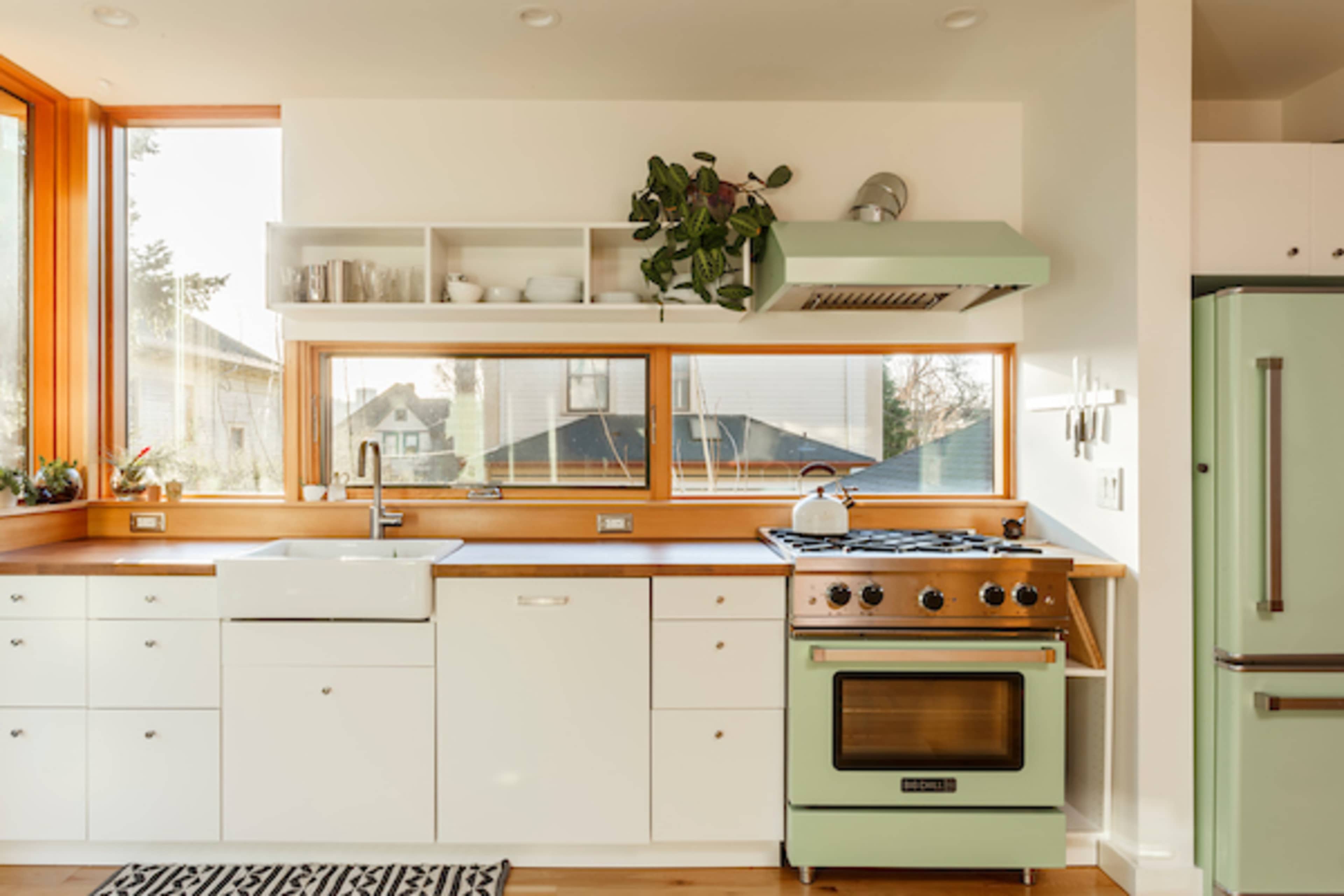 The kitchen features a white countertop, a green vintage-style stove, a farmhouse sink, and large windows that illuminate the space.