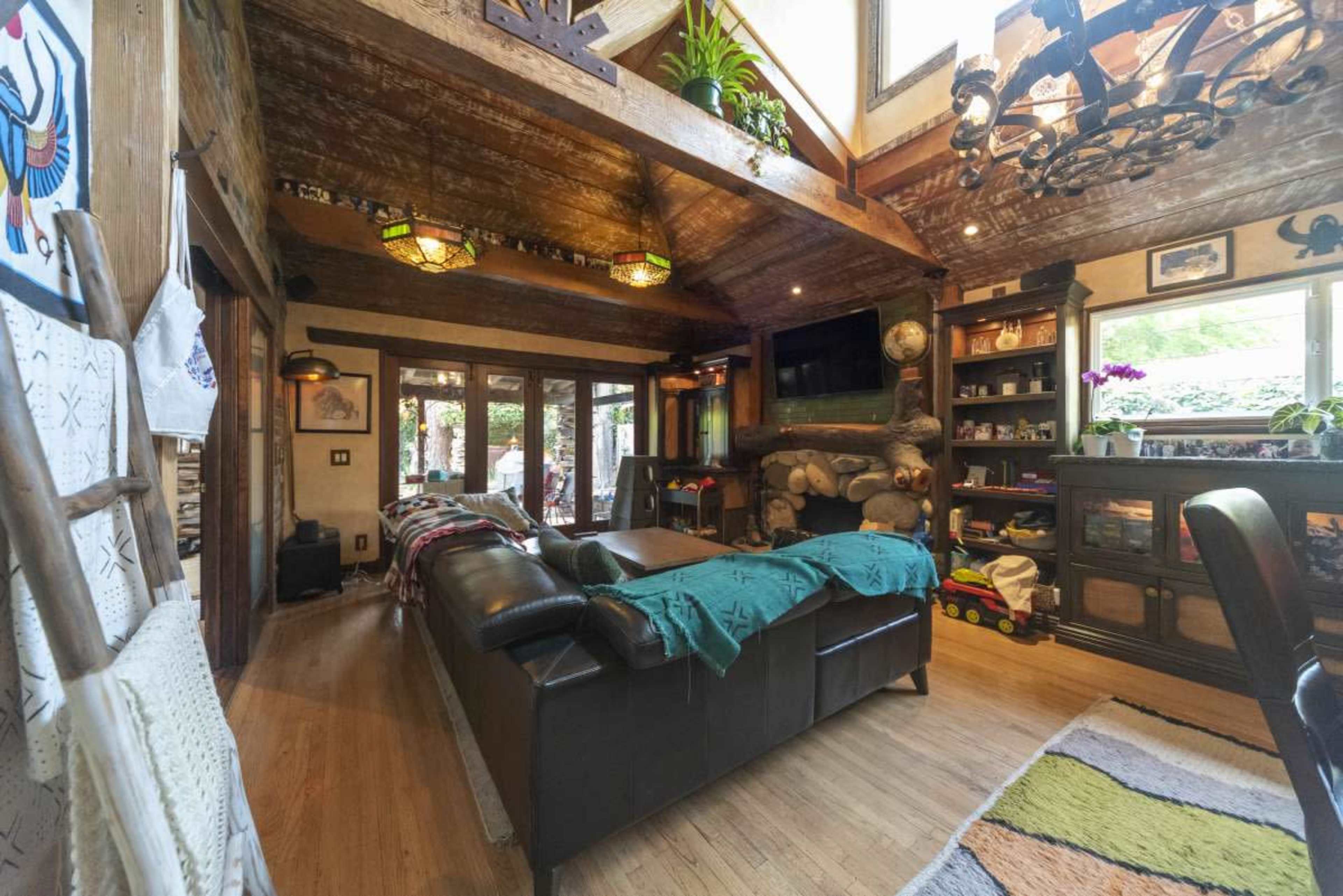 A cozy living room features a leather sofa, wooden beams on the ceiling, and large windows allowing natural light to fill the space.