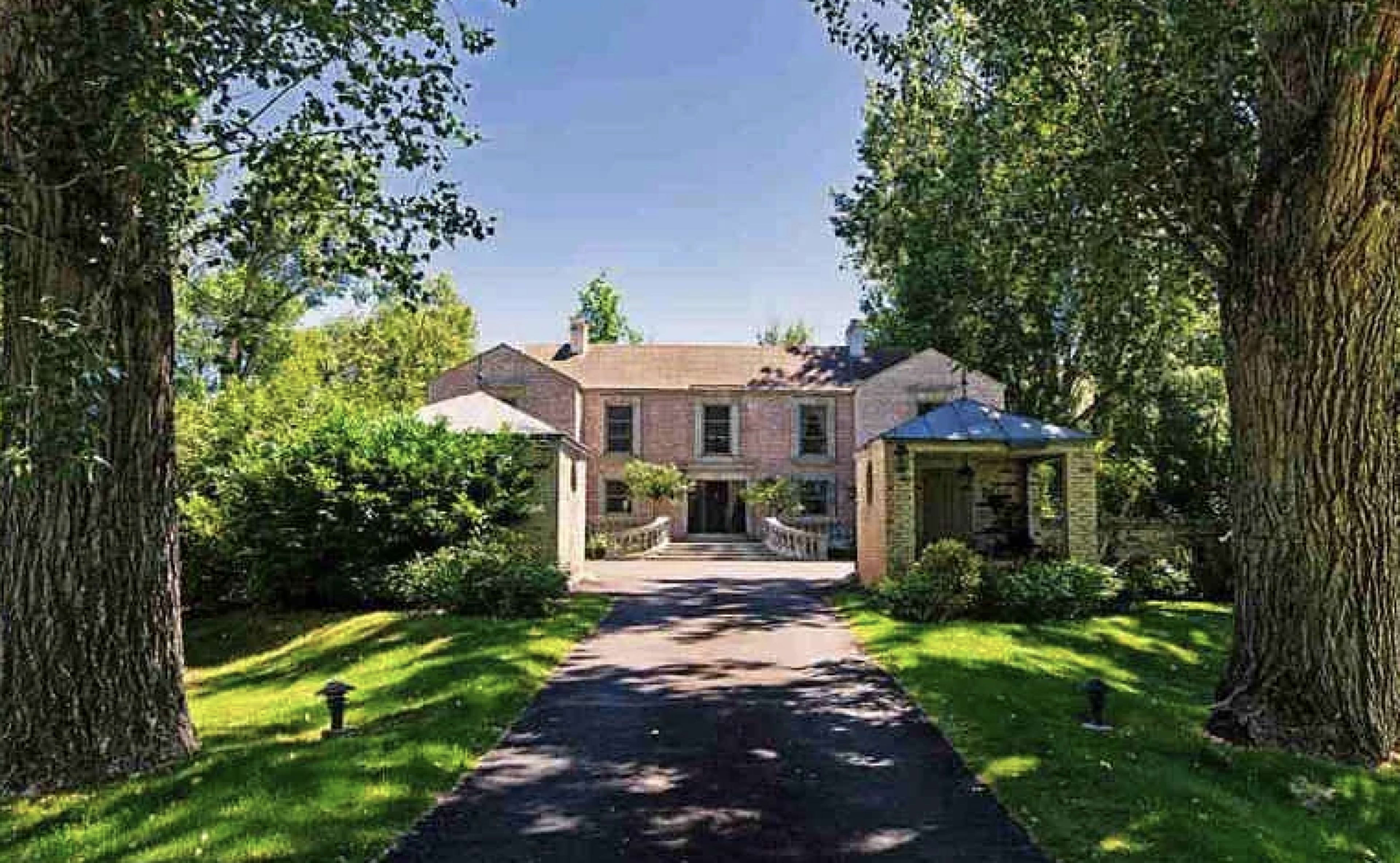 A large, two-story house is framed by tall trees and surrounded by a well-manicured lawn.