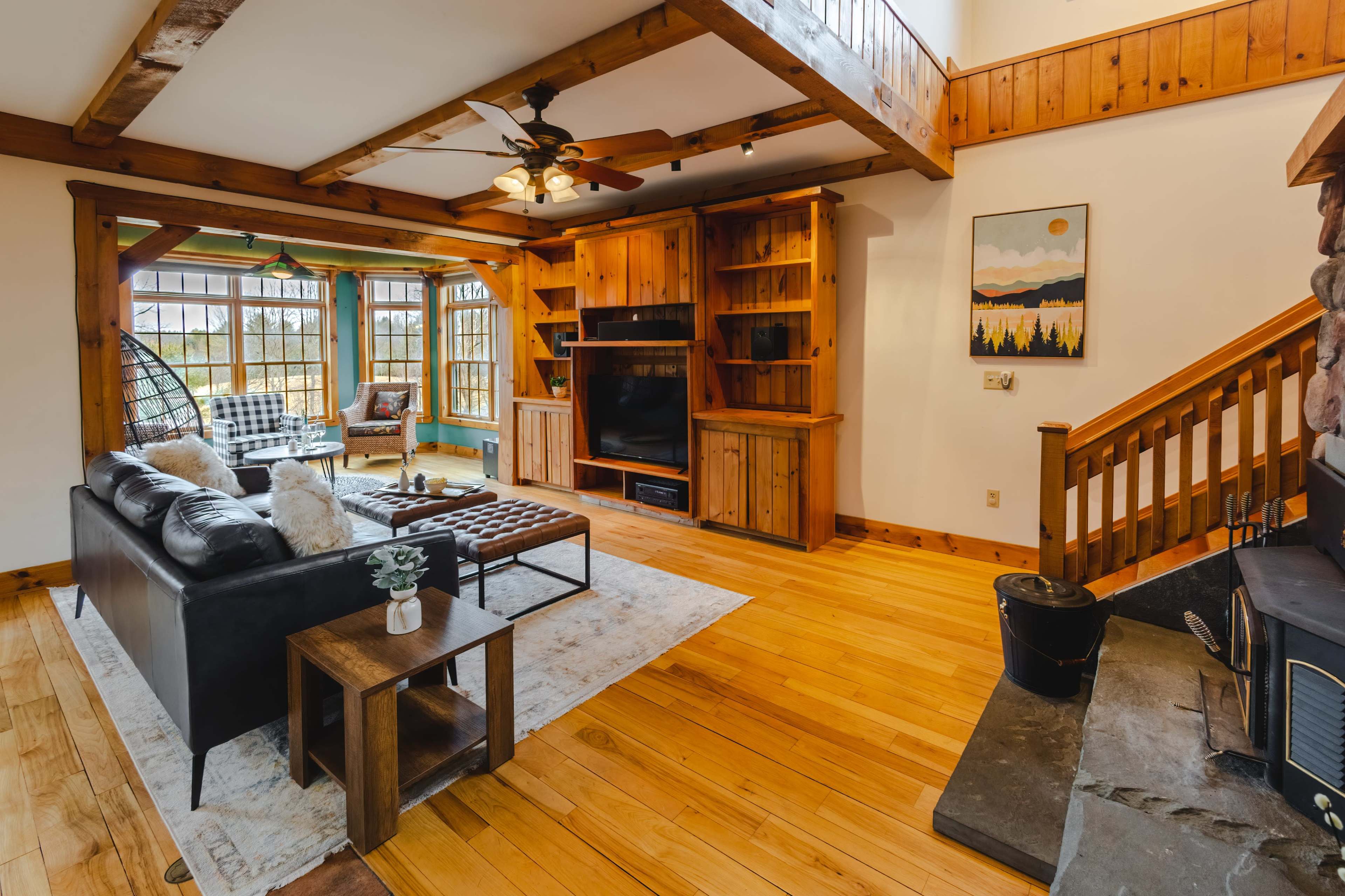 A cozy living room with a wooden ceiling, a black leather sofa, a coffee table, built-in shelves, and a fireplace.