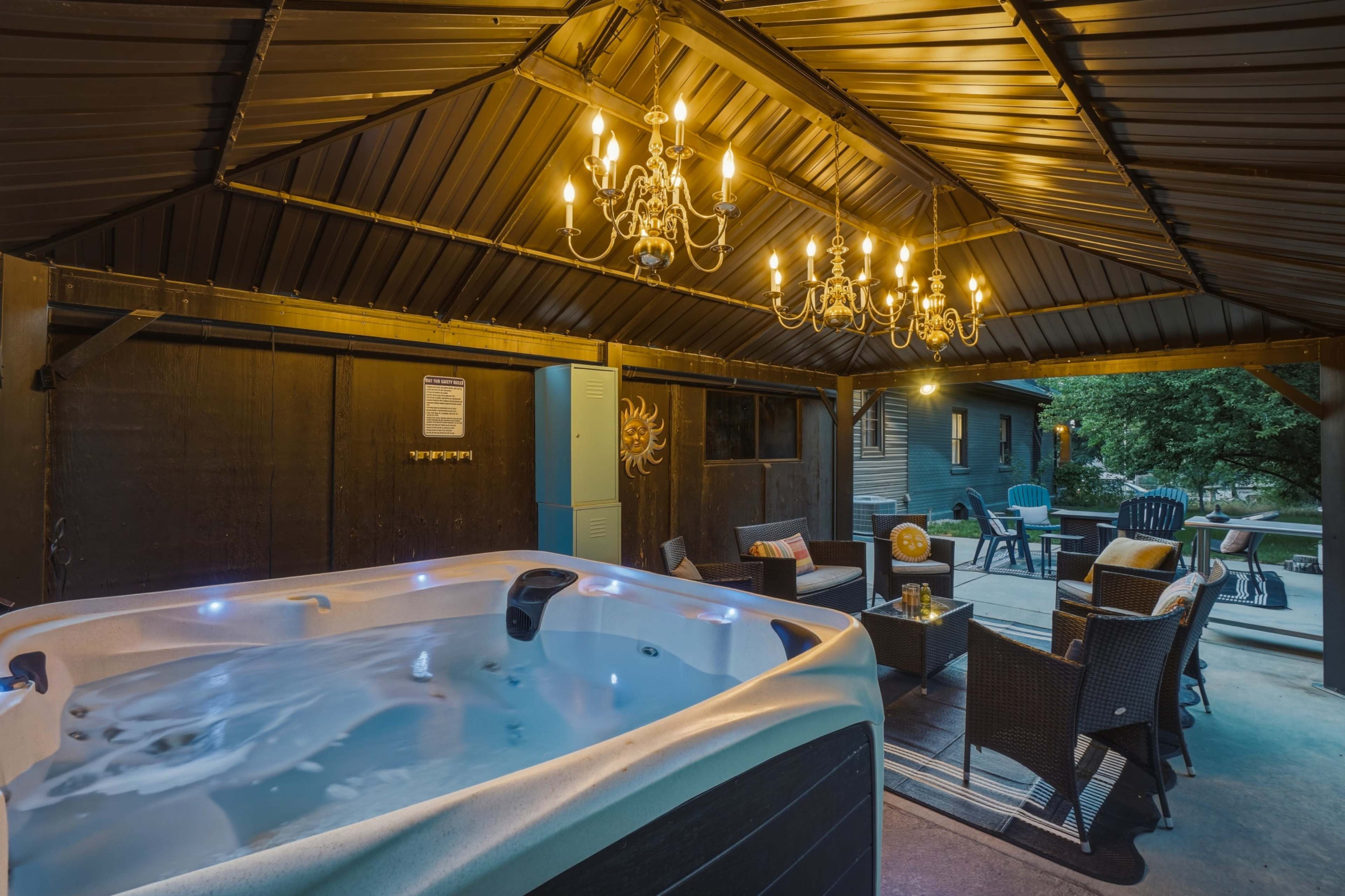 A hot tub is situated under a covered patio with a chandelier, surrounded by seating arrangements.