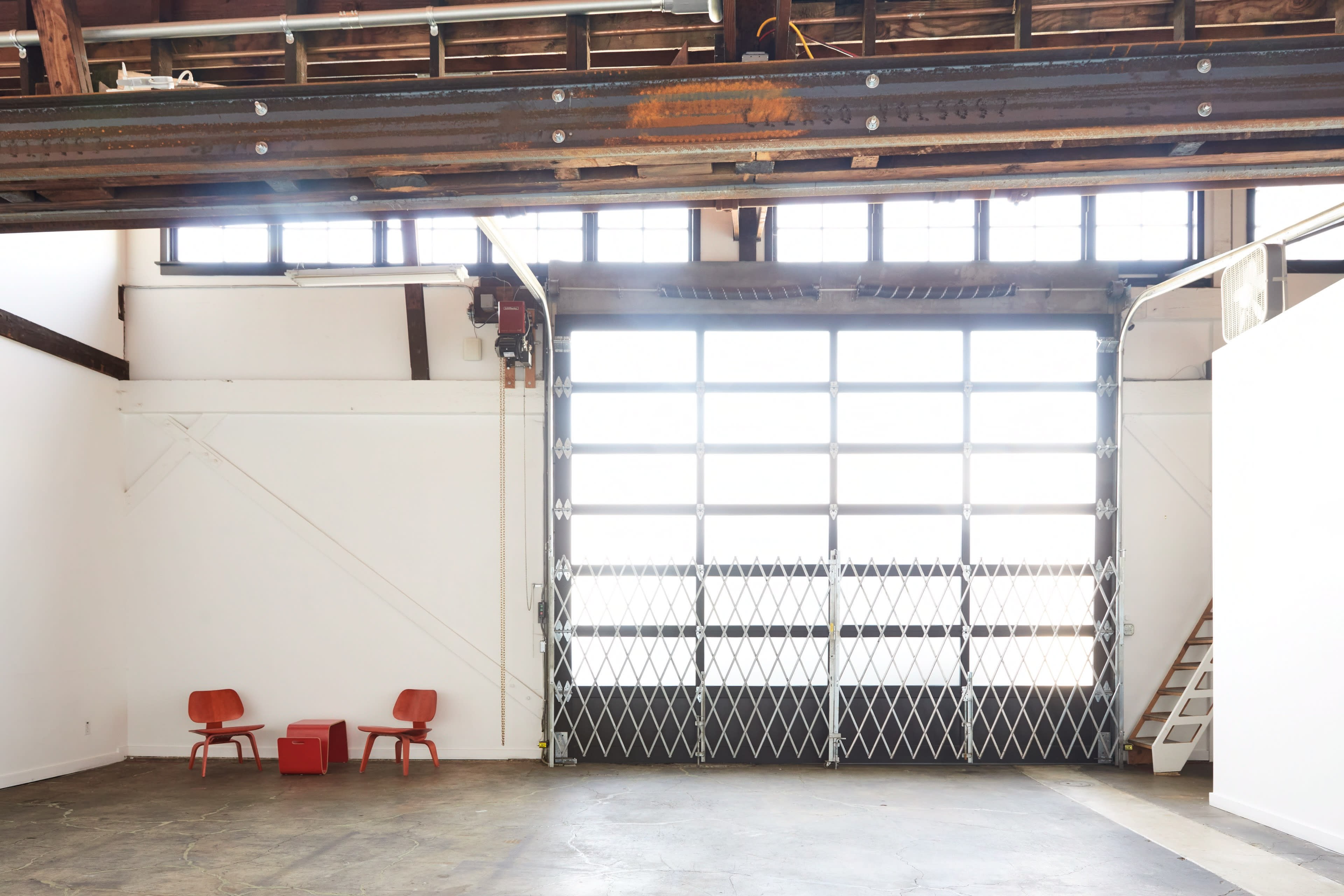 An open industrial space features two red chairs and a large glass garage door that leads outside.