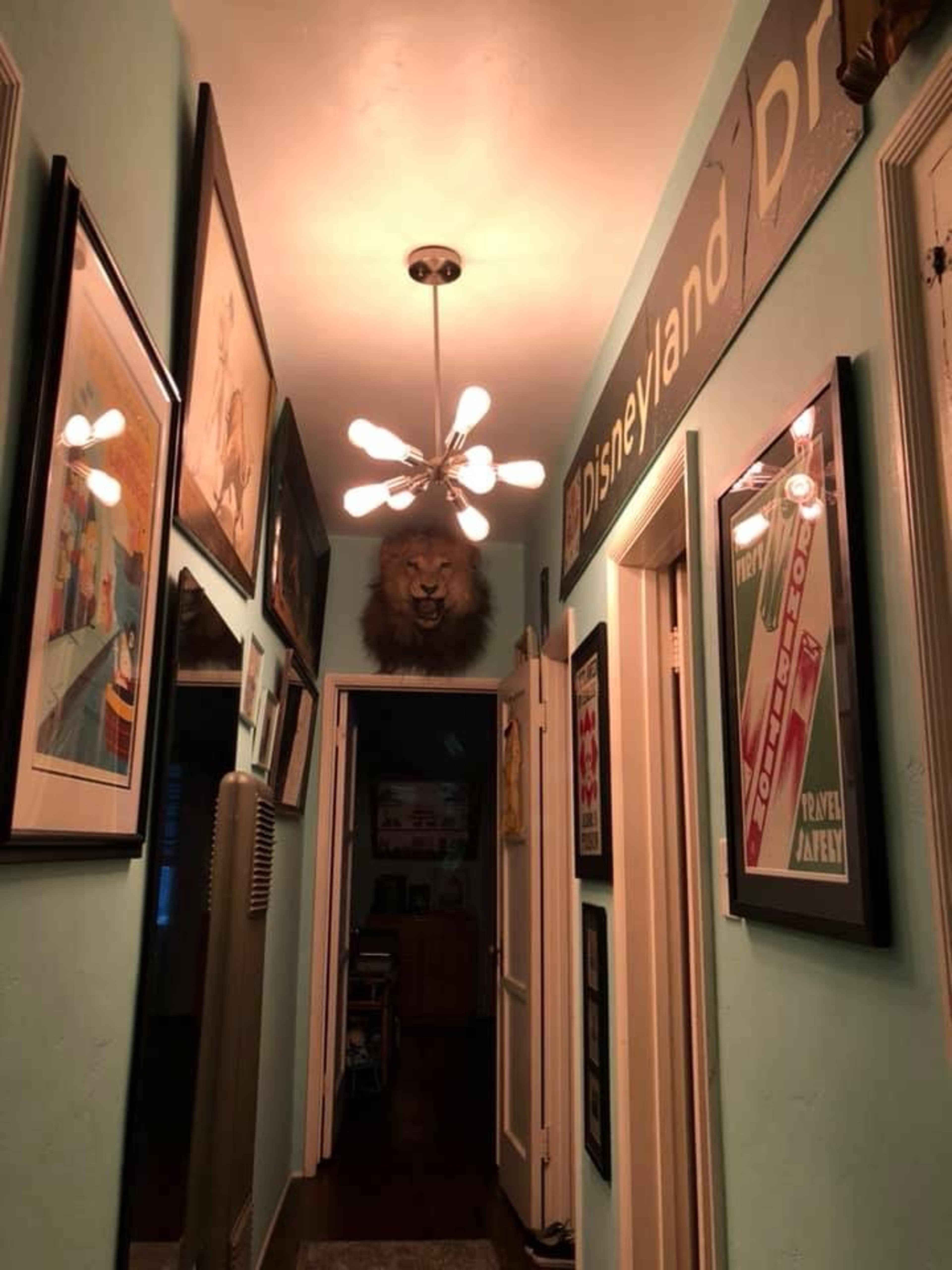 A hallway is decorated with framed art on both sides, leading to a door at the end and featuring a mounted lion's head near the ceiling.