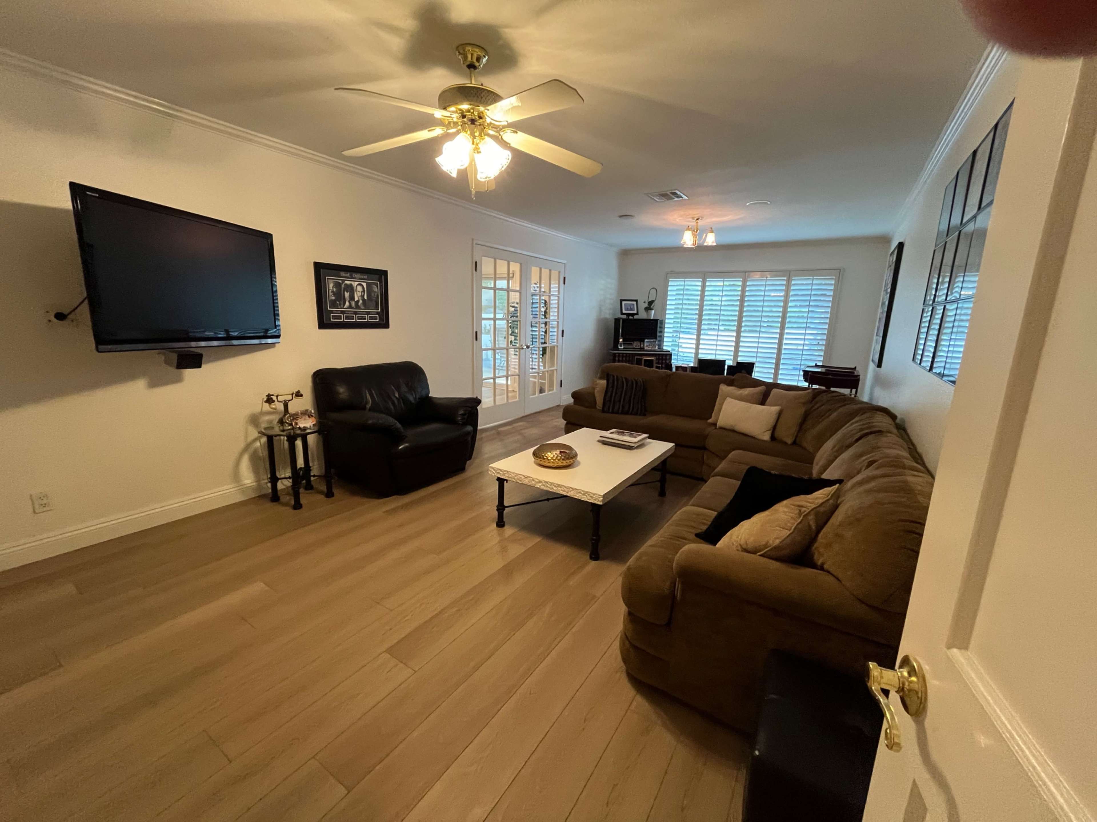The image shows a living room featuring a large brown sectional sofa, a black leather chair, a white coffee table, and a wall-mounted television.