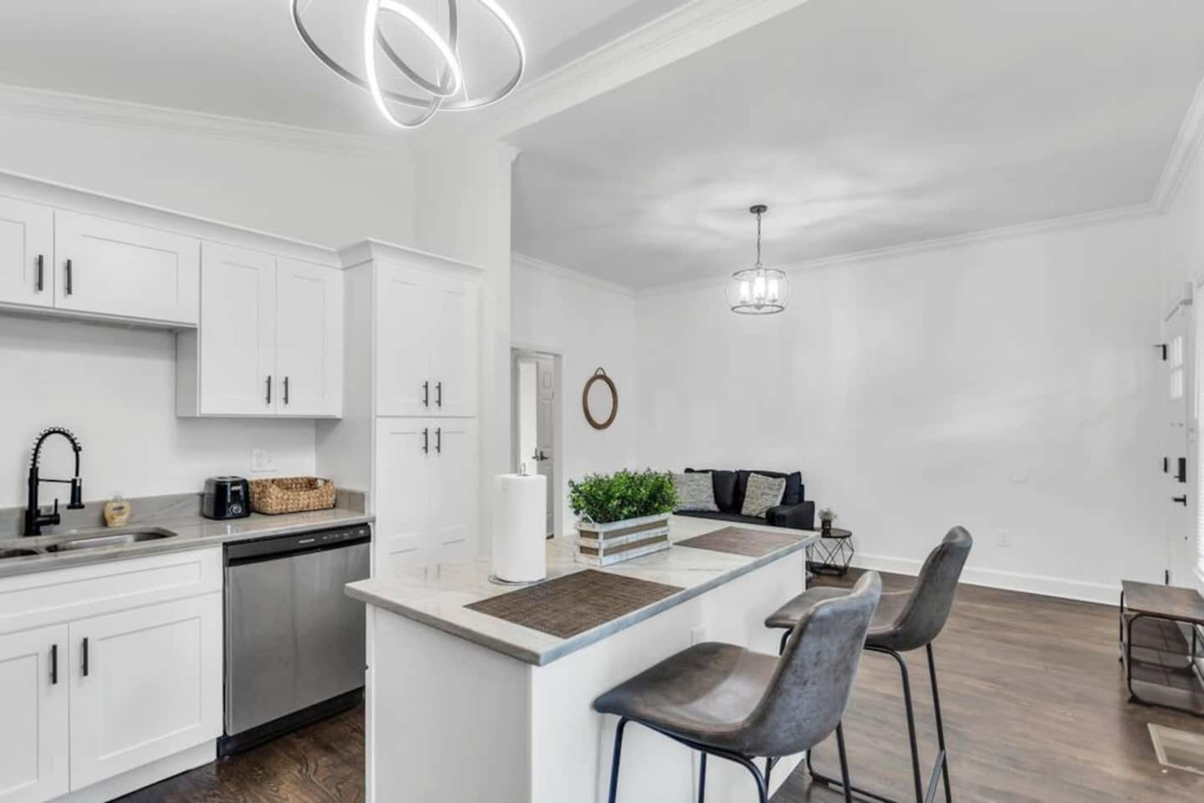 A modern kitchen with white cabinetry, a kitchen island with bar stools, and a living area featuring a sofa and decorative elements.