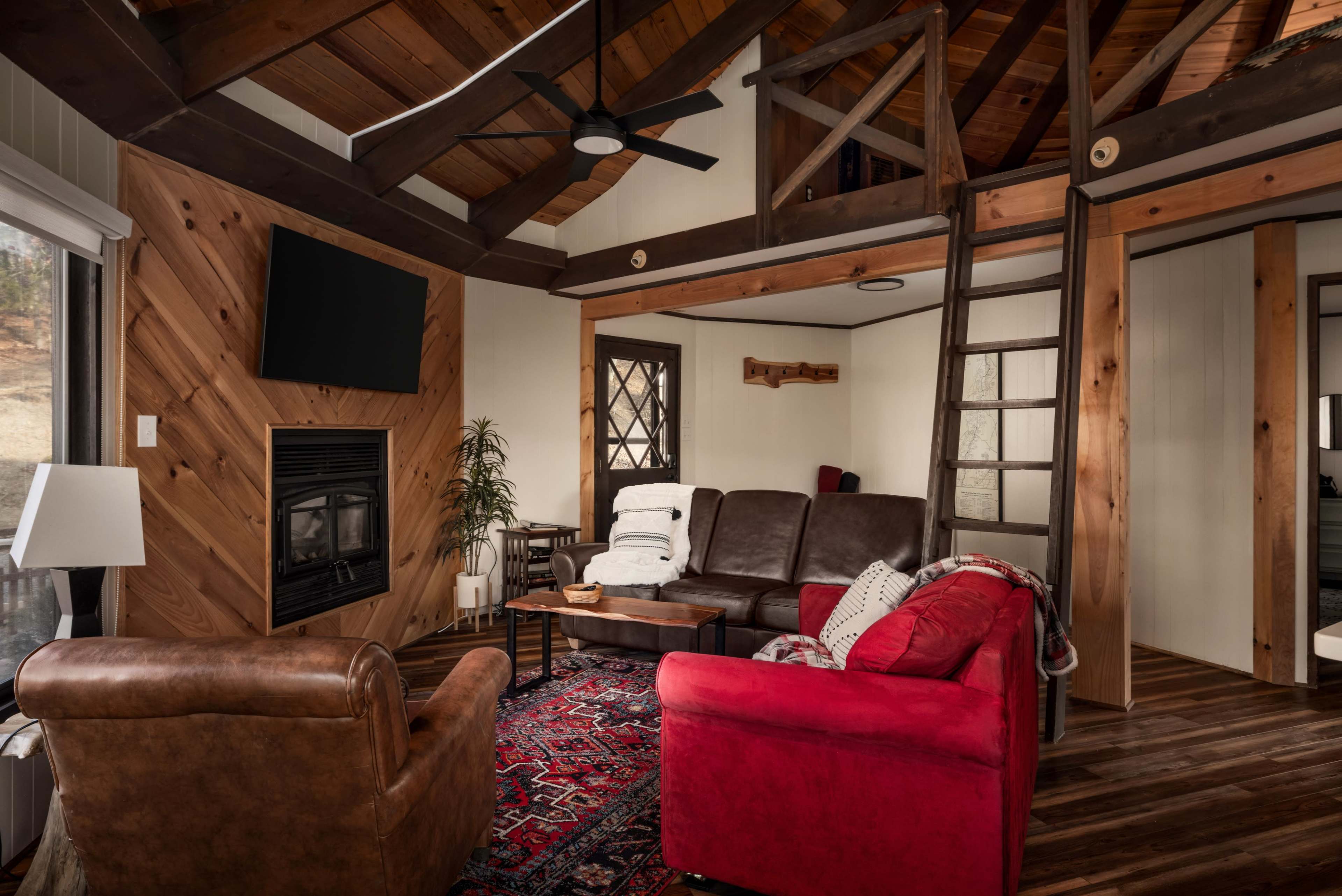 The room features a cozy living area with a leather couch, a red armchair, a fireplace, and exposed wooden beams on the ceiling.