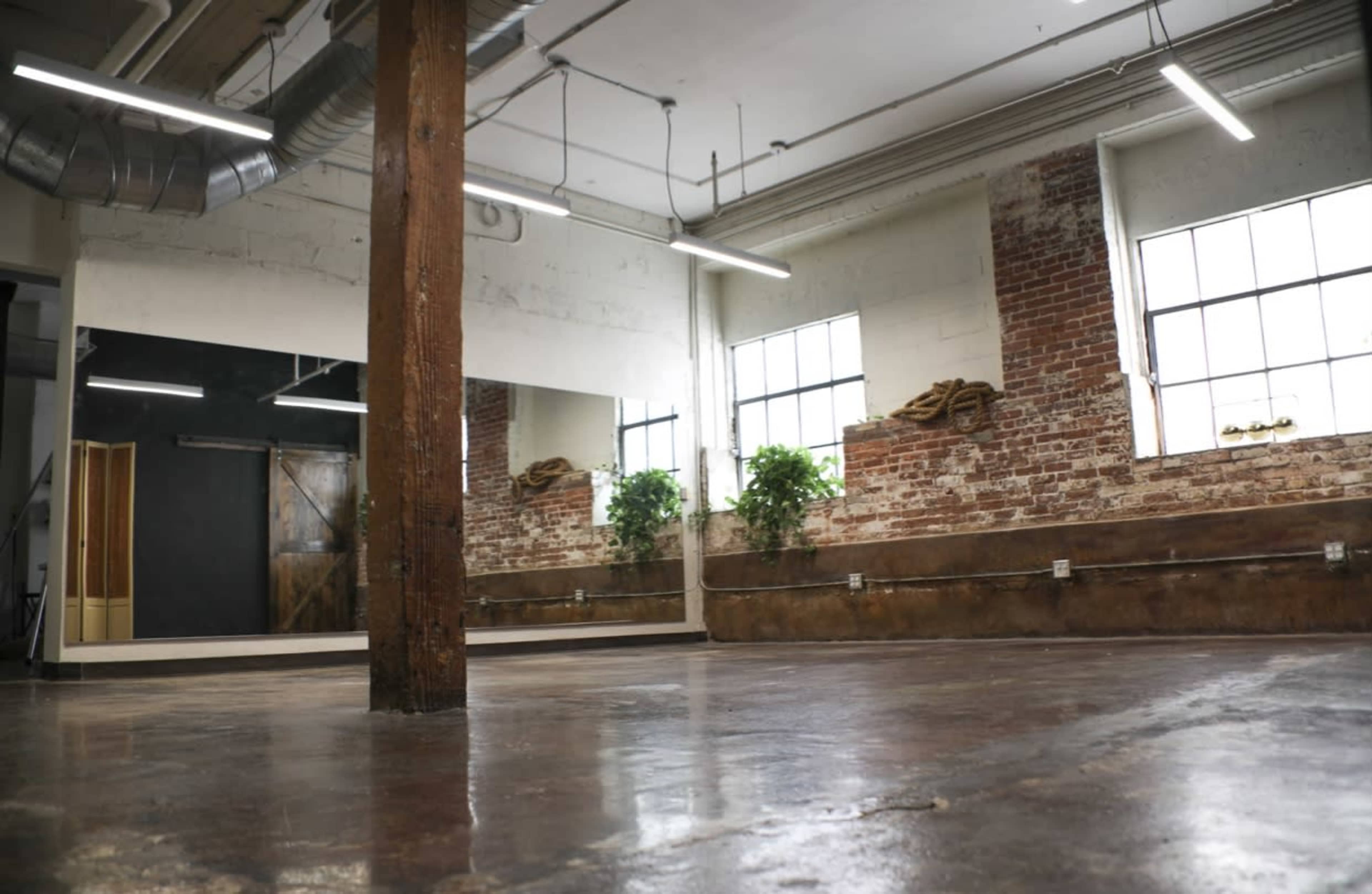A spacious room with a polished concrete floor, exposed brick walls, and a large mirror reflecting the interior.
