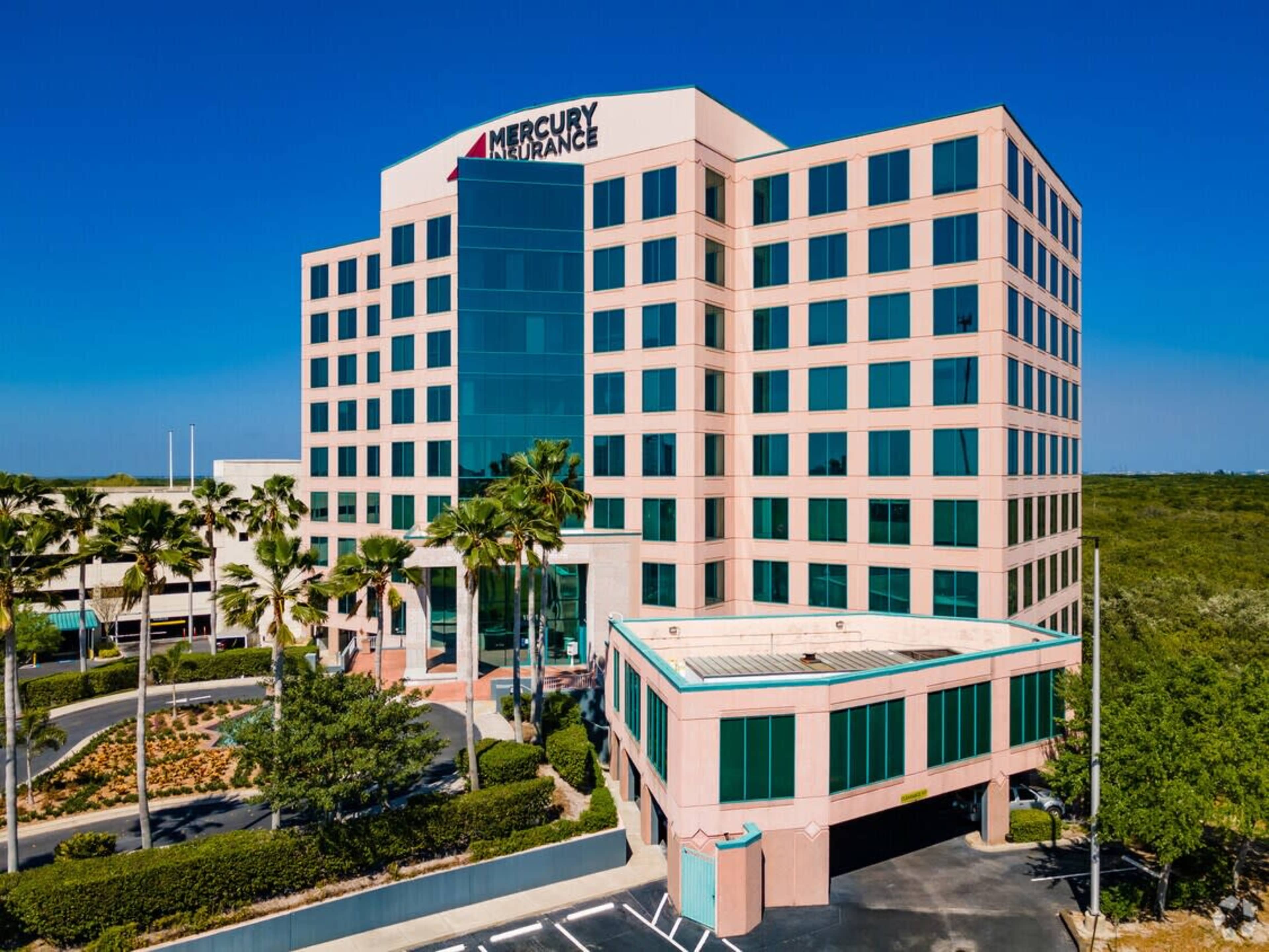 The image shows a modern, multi-story office building with large windows and the Mercury Insurance logo prominently displayed on the roof, surrounded by palm trees and landscaped grounds.
