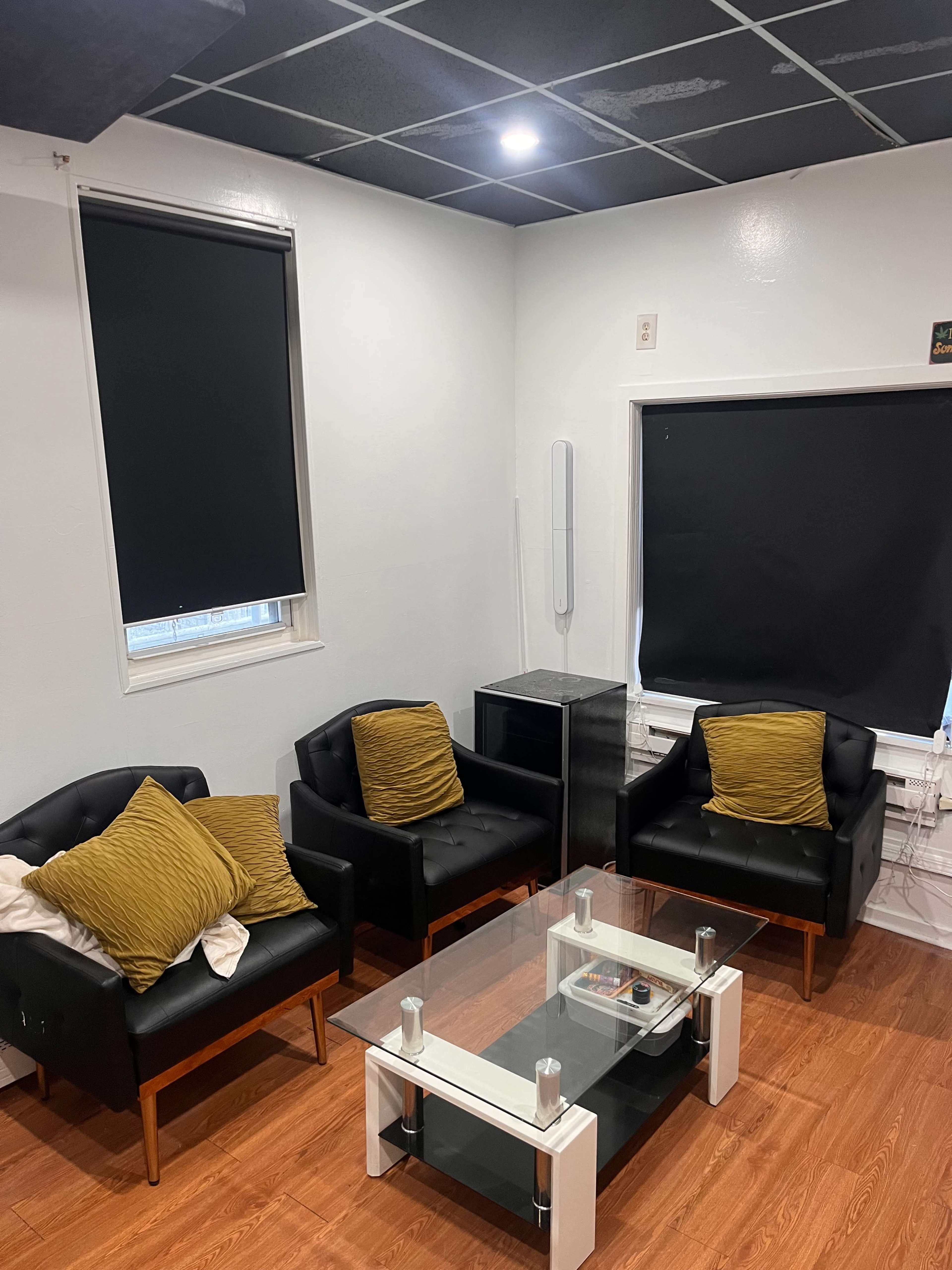 The image shows a small, modern lounge area with two black armchairs and a glass coffee table on a wooden floor.