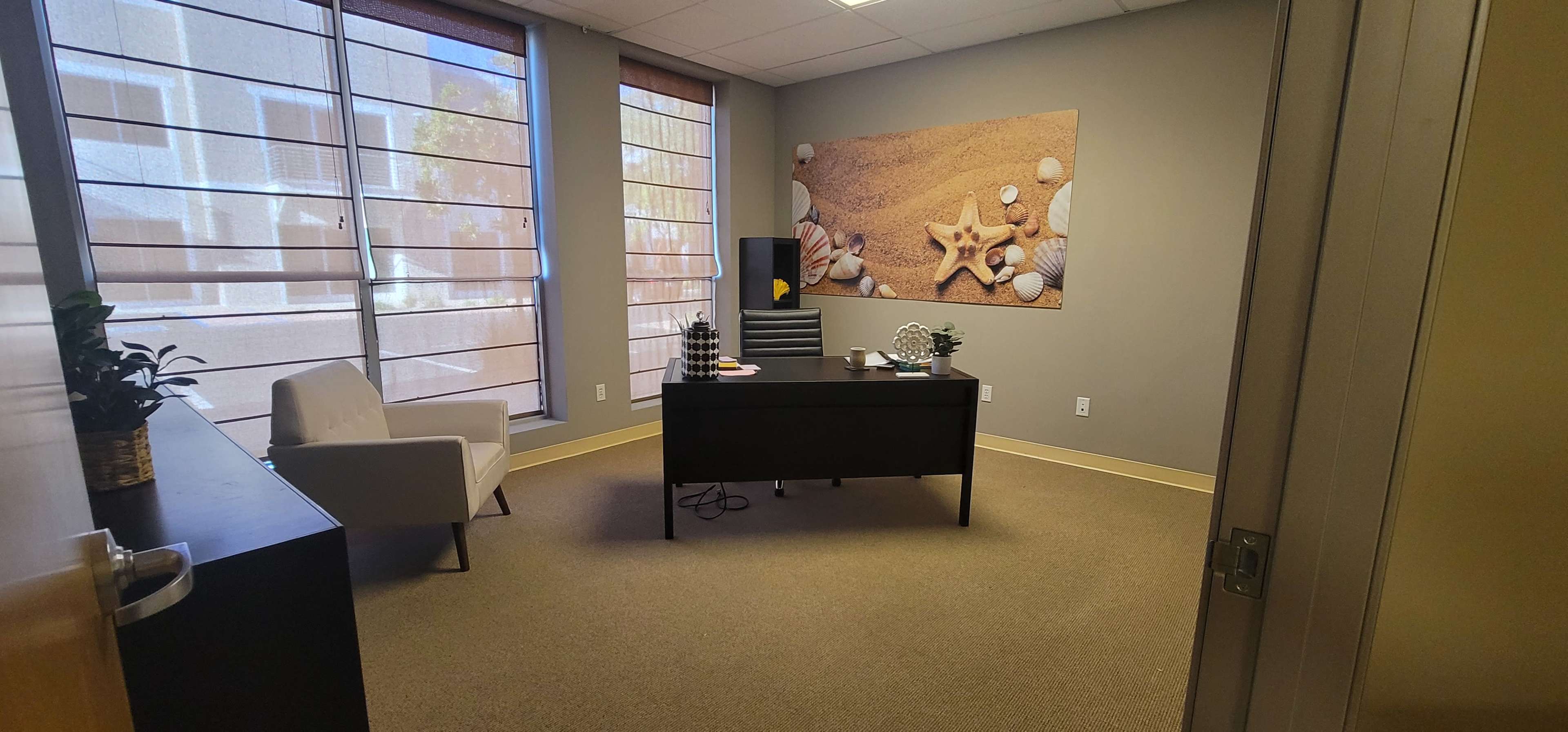 A modern office space featuring a desk, a white chair, and a wall decoration with seashells and a starfish.