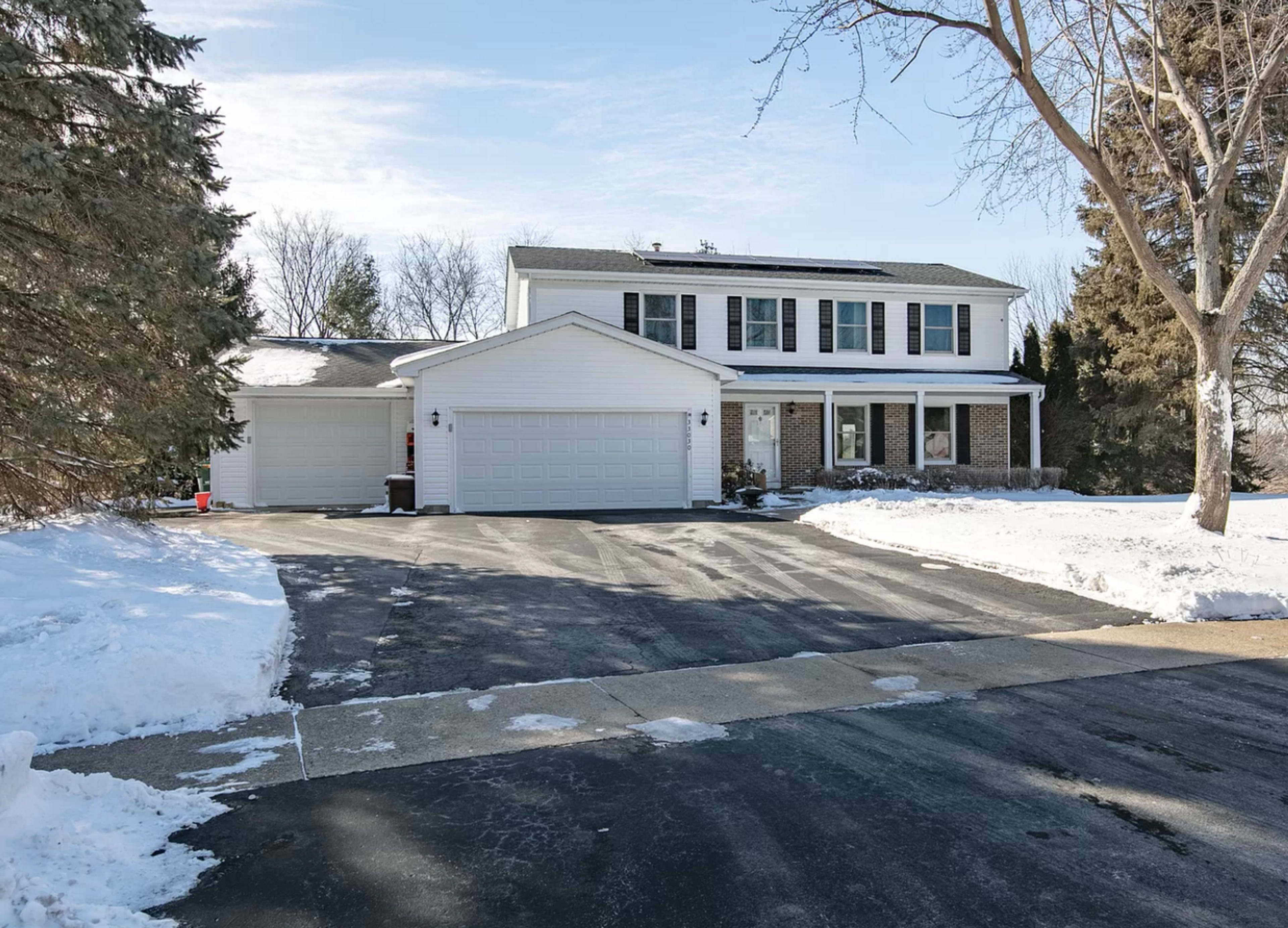 A two-story house with a spacious driveway and snow-covered landscaping is shown.