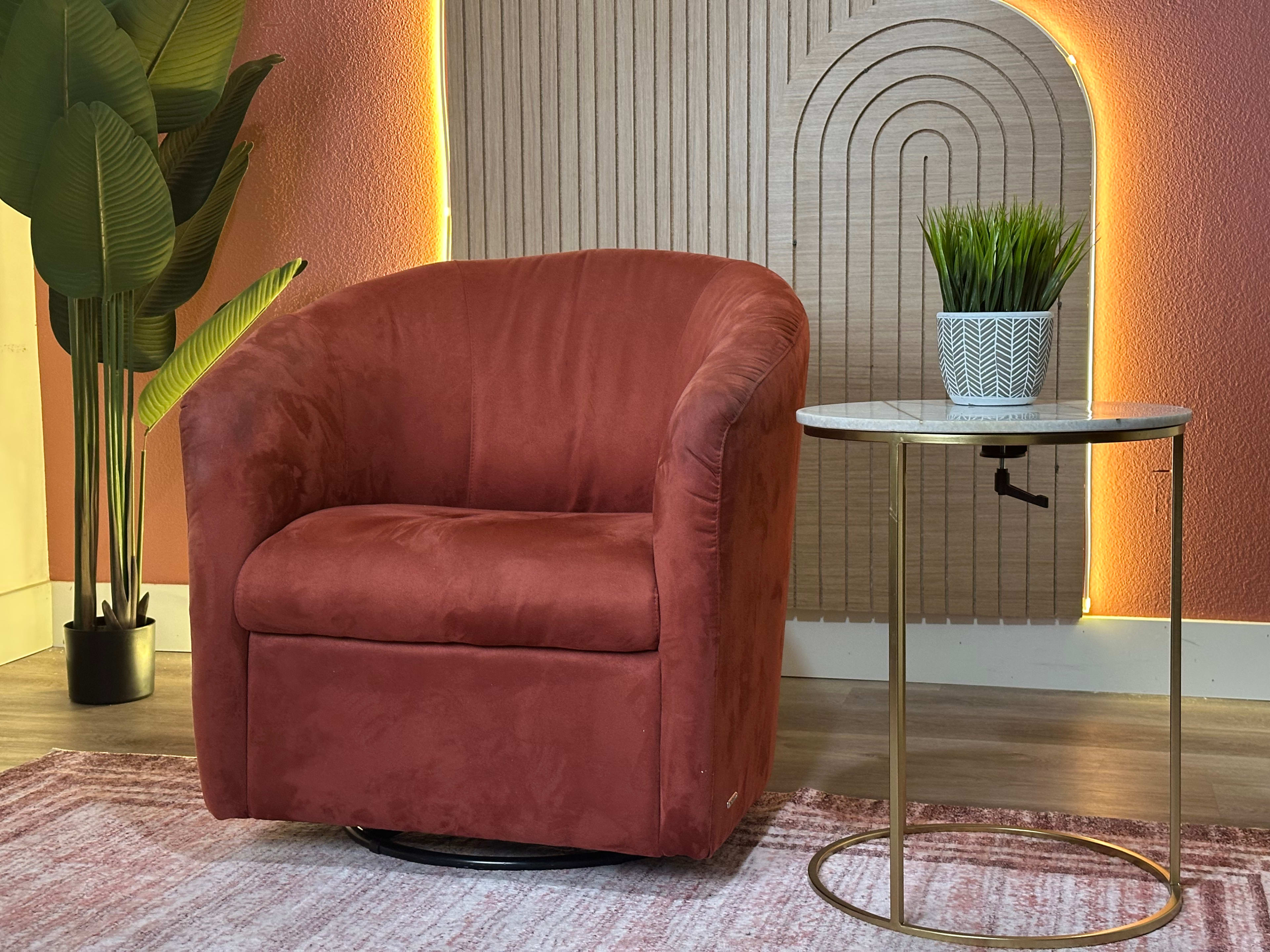 The image shows a cozy, reddish-brown armchair next to a small round table with a potted plant on it, set against a backdrop of textured wall panels and soft lighting.