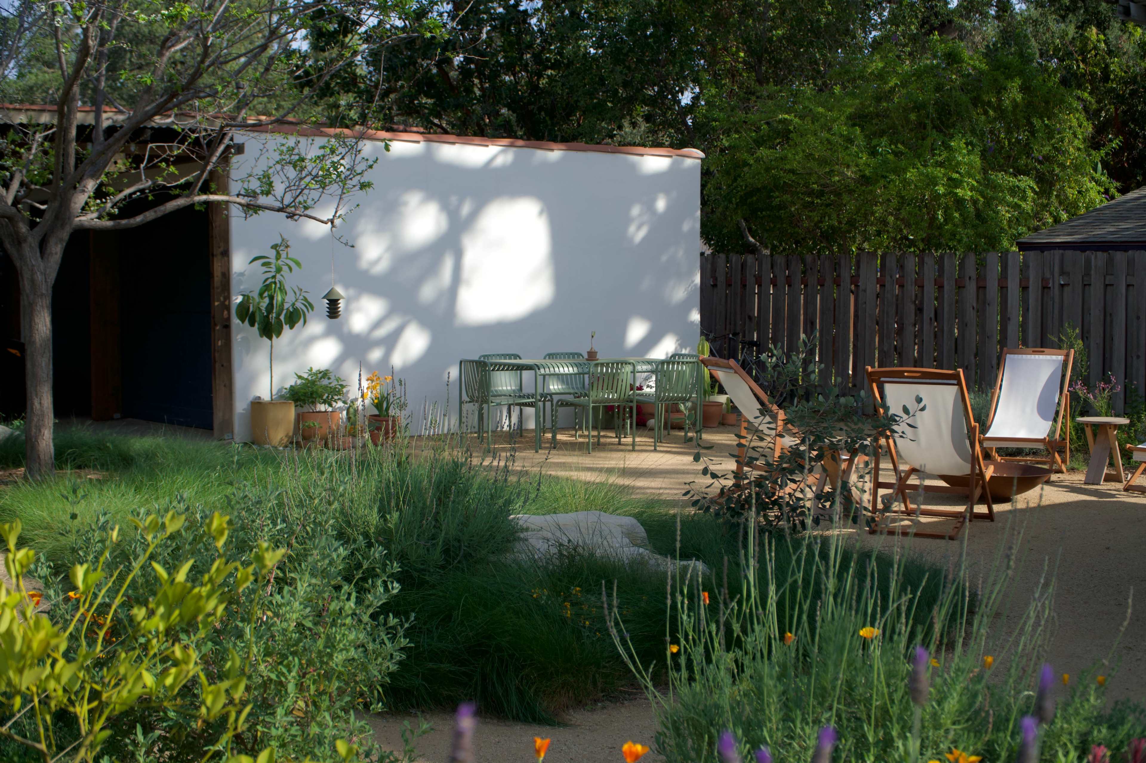 The image shows a small outdoor garden area with a white wall, green furniture, and various plants.