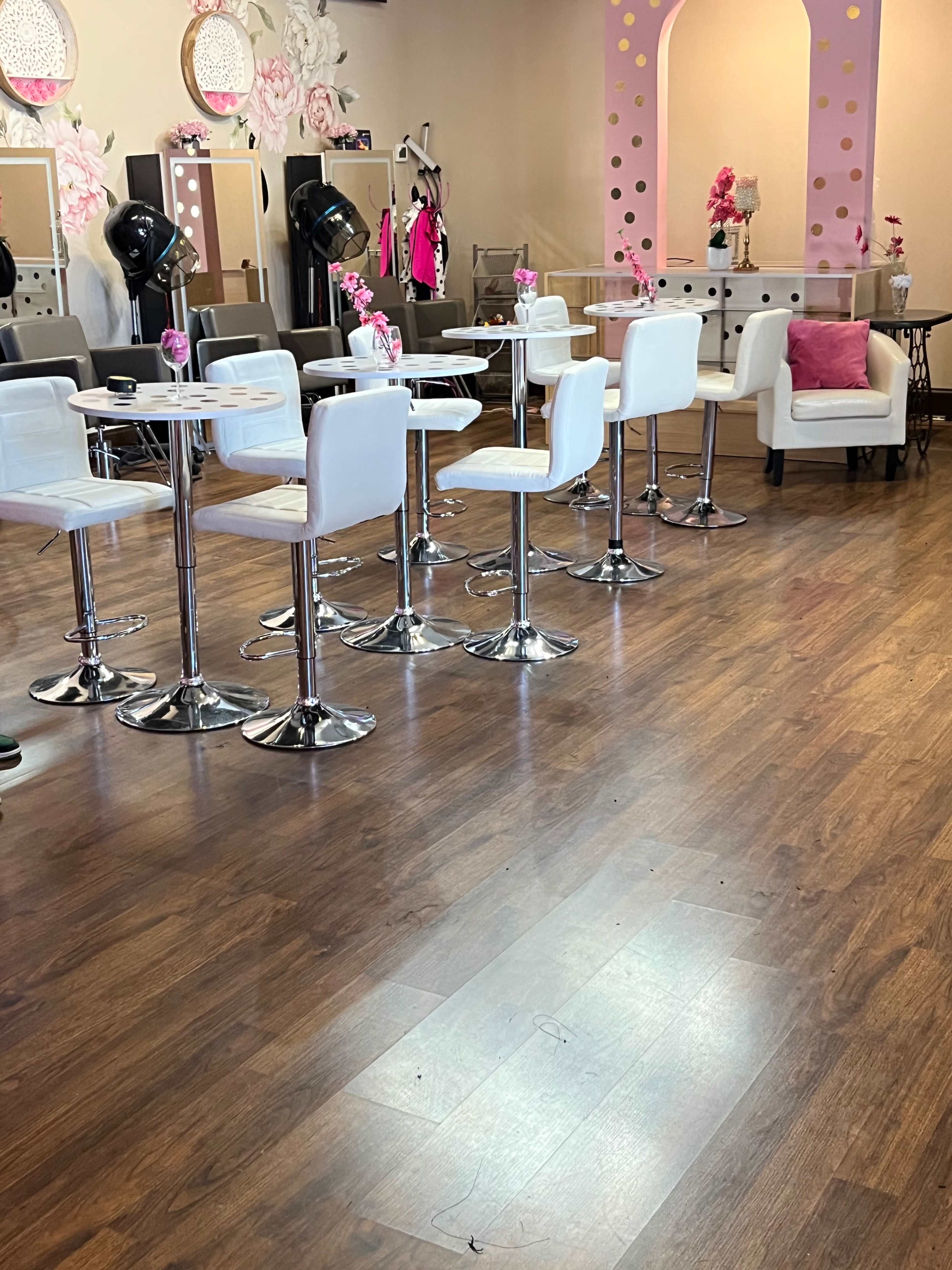 A salon interior featuring white barstools at tables, surrounded by mirrors and decorative elements.