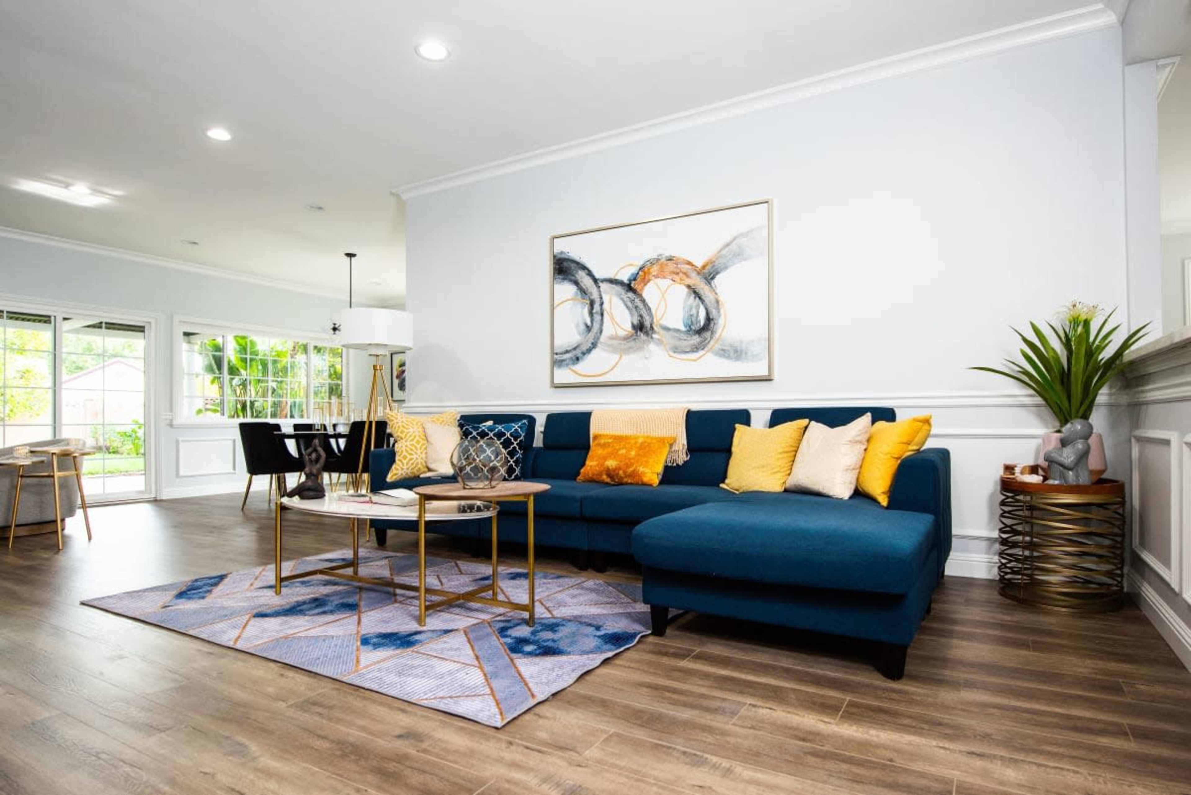 A modern living room features a blue sectional sofa adorned with yellow pillows, a geometric rug, and a wall art piece above a coffee table.