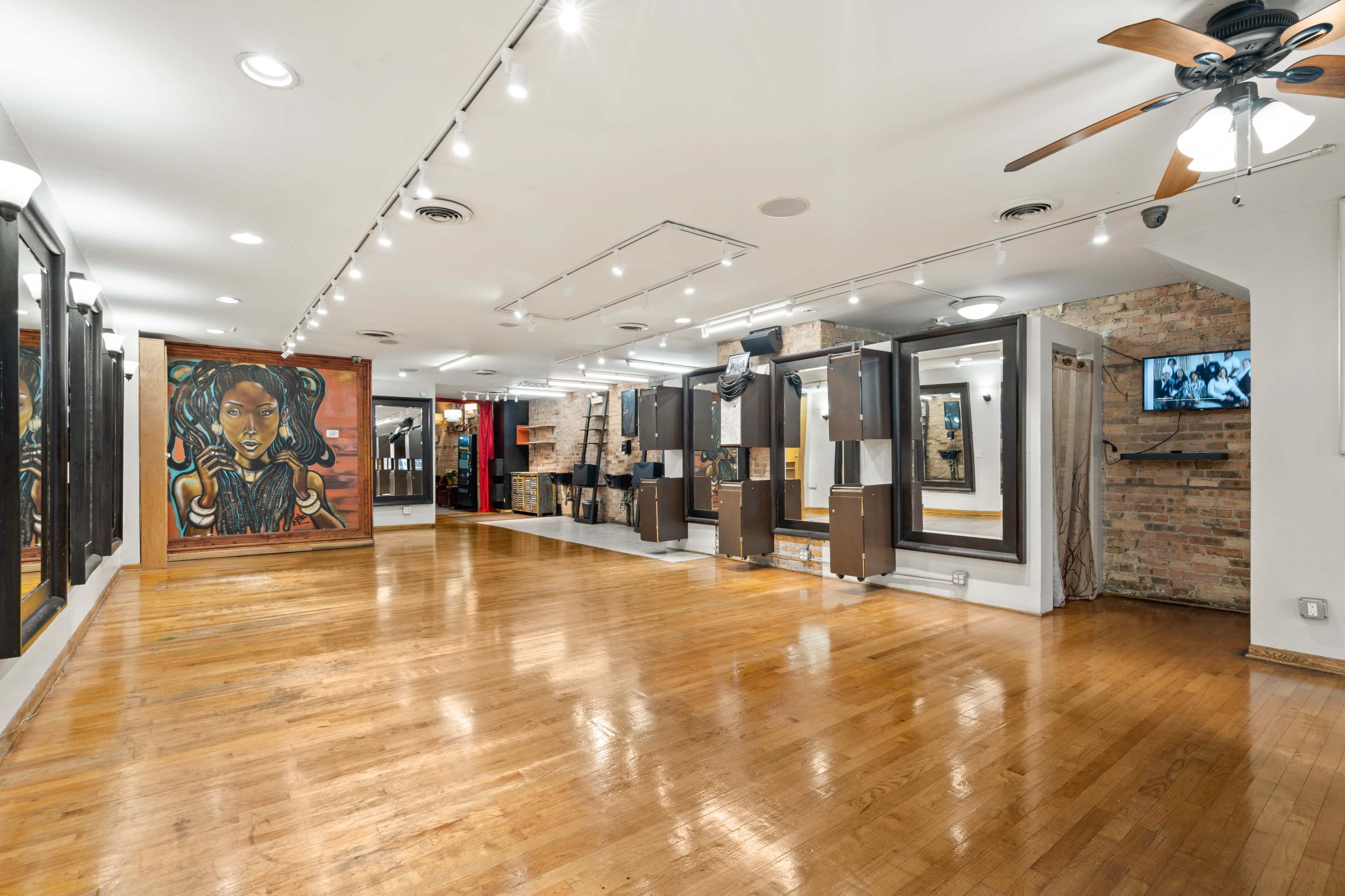 The image shows a spacious art gallery with wooden floors, rows of display panels, and a large mural on one wall.