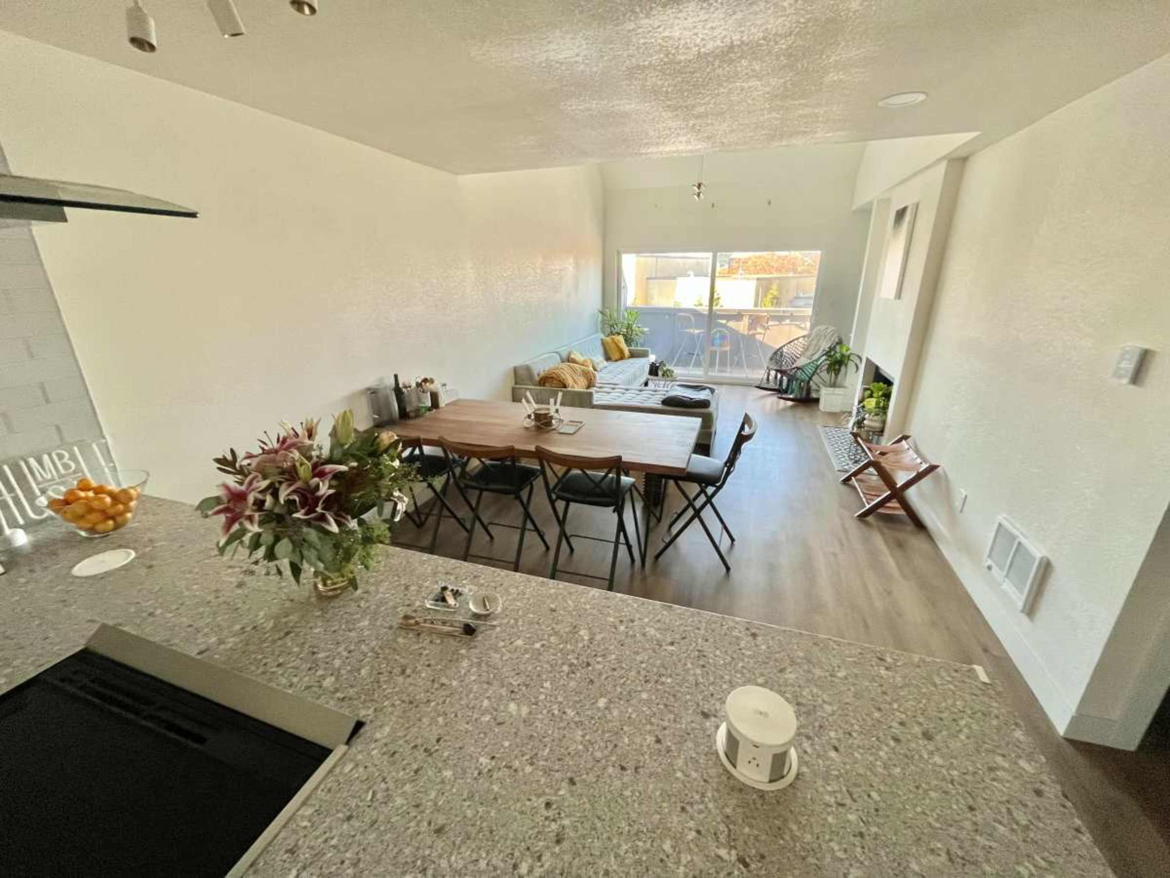 A modern living space features a dining table with chairs, a sofa, and large windows that allow natural light to enter.