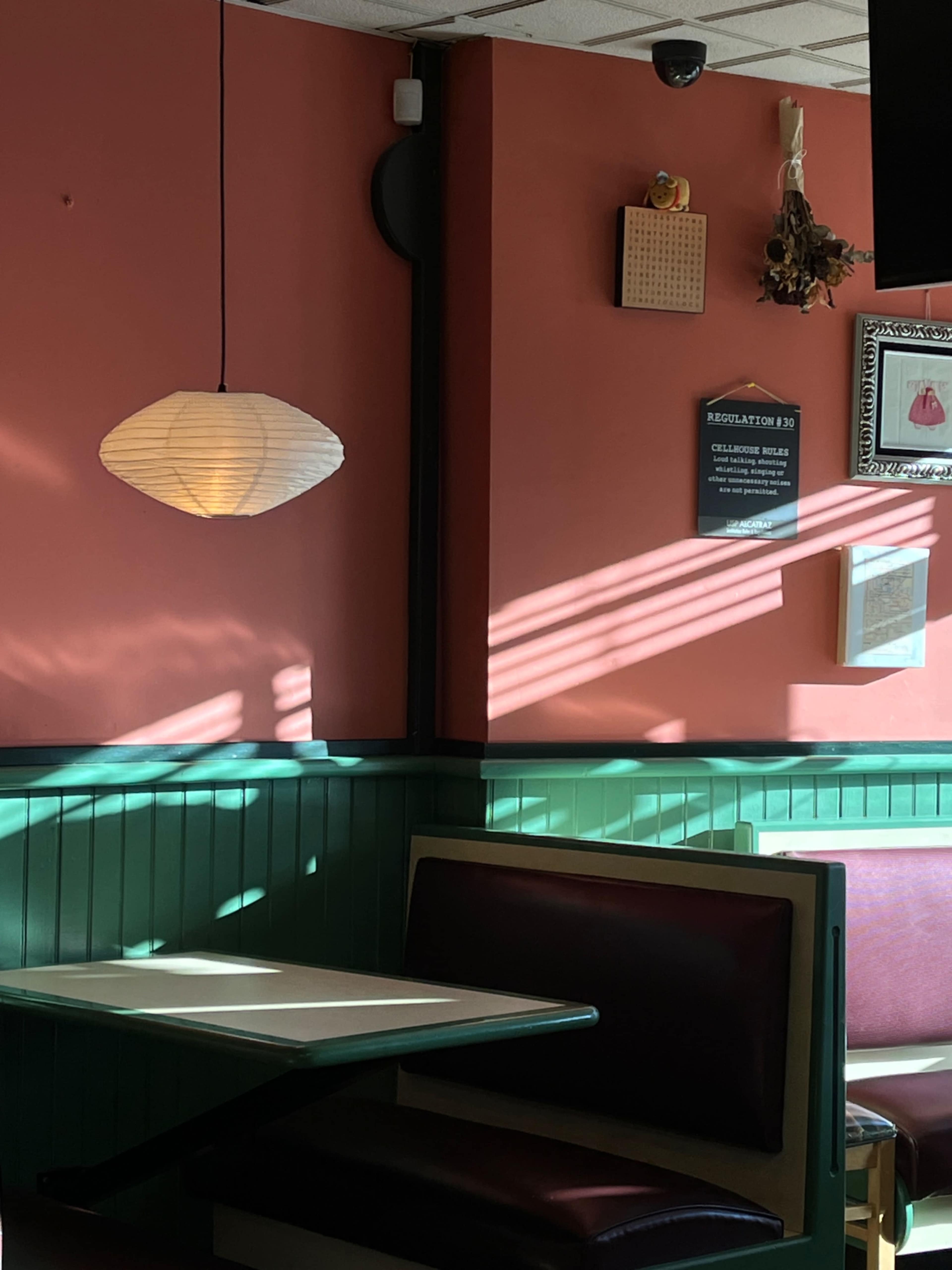 A corner of a restaurant featuring a paper lantern, a green wainscoted wall, and a table with red upholstered seating.