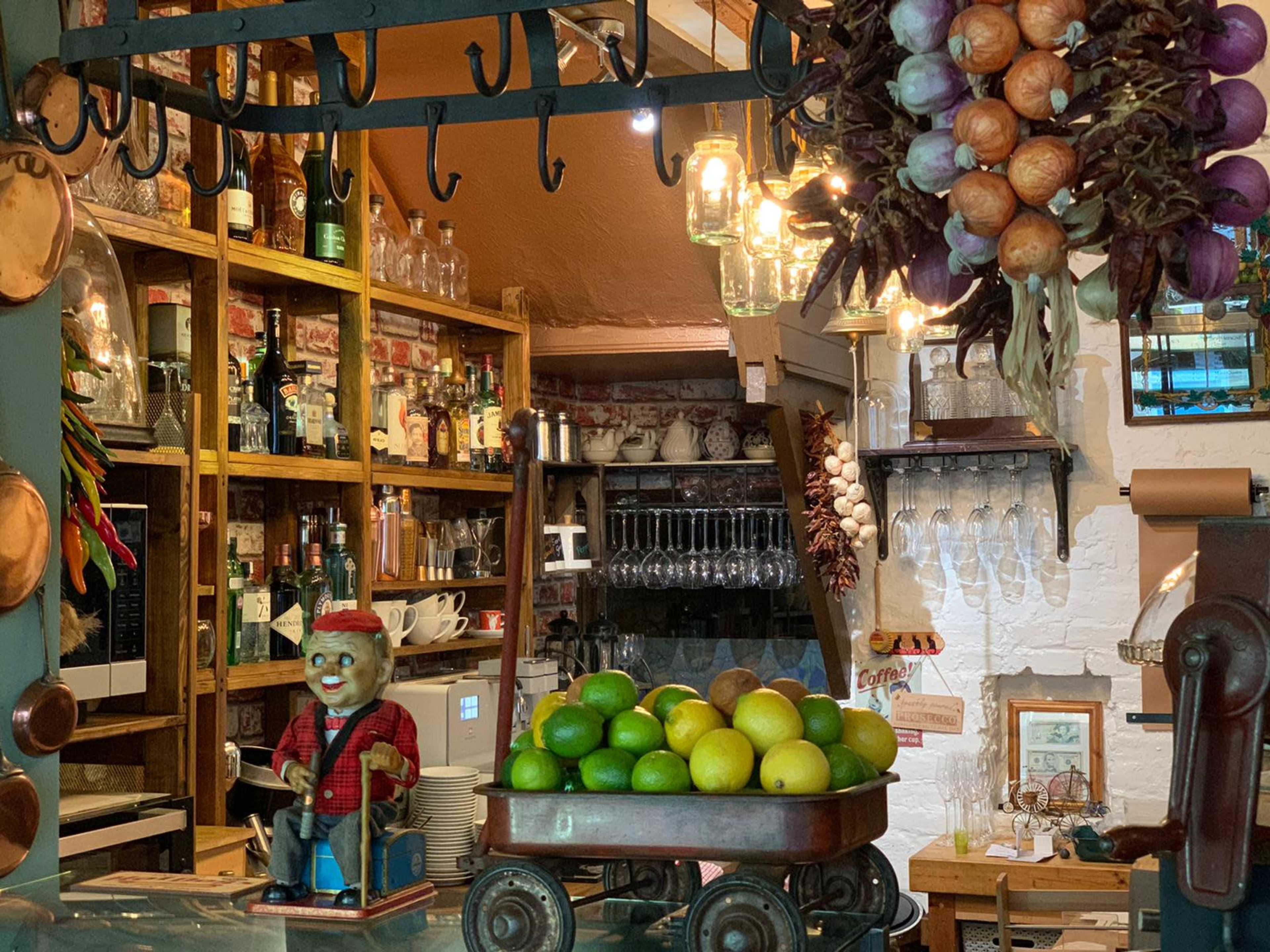 A quaint bar area featuring shelves filled with bottles, a decorative statue, and a wheelbarrow carrying fresh limes and lemons.