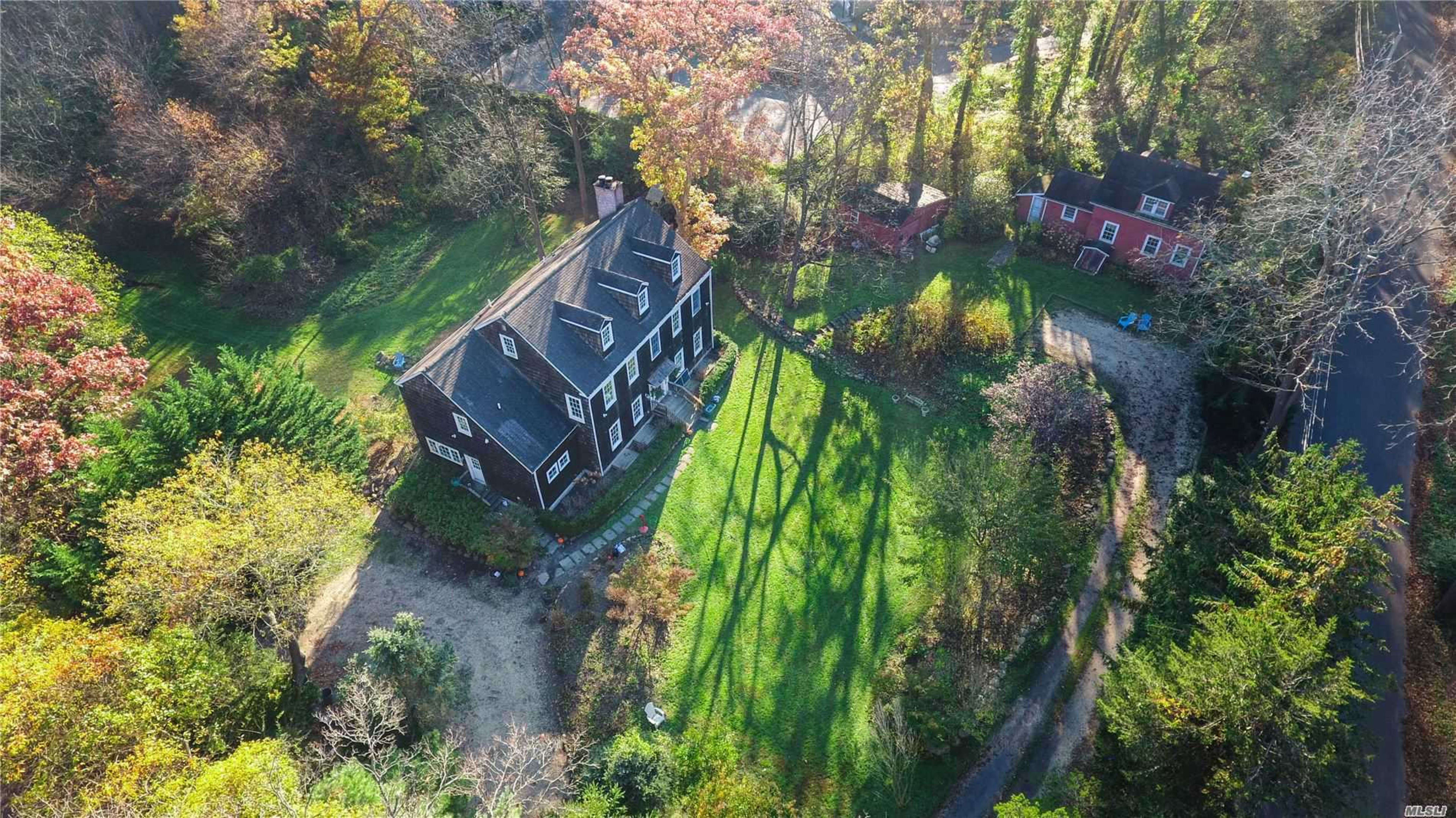 An aerial view shows a large black house surrounded by green lawns and trees, with a smaller red house visible in the background.