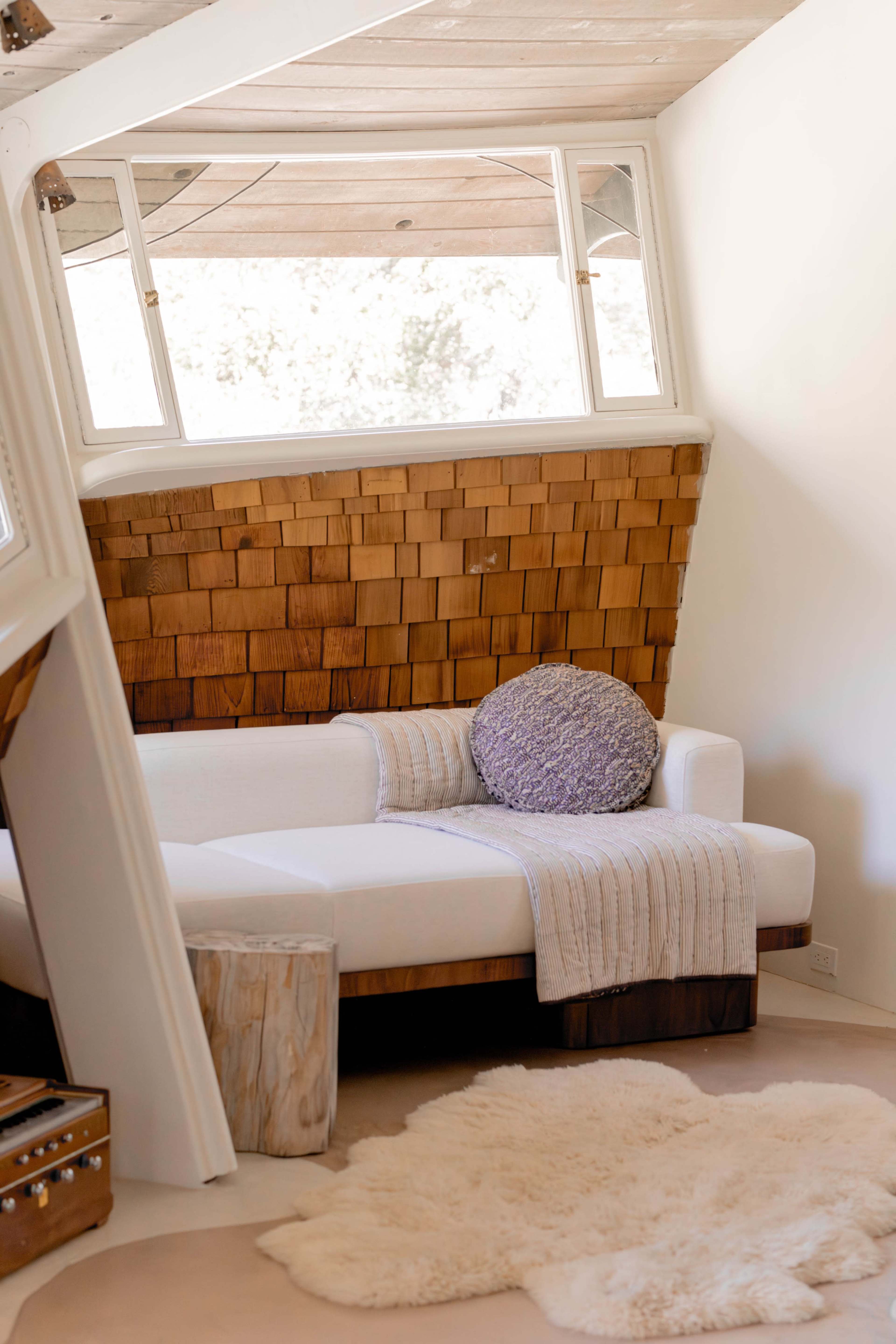 The image shows a cozy living space with a white couch, a round purple pillow, a wooden side table, and a soft rug on the floor.