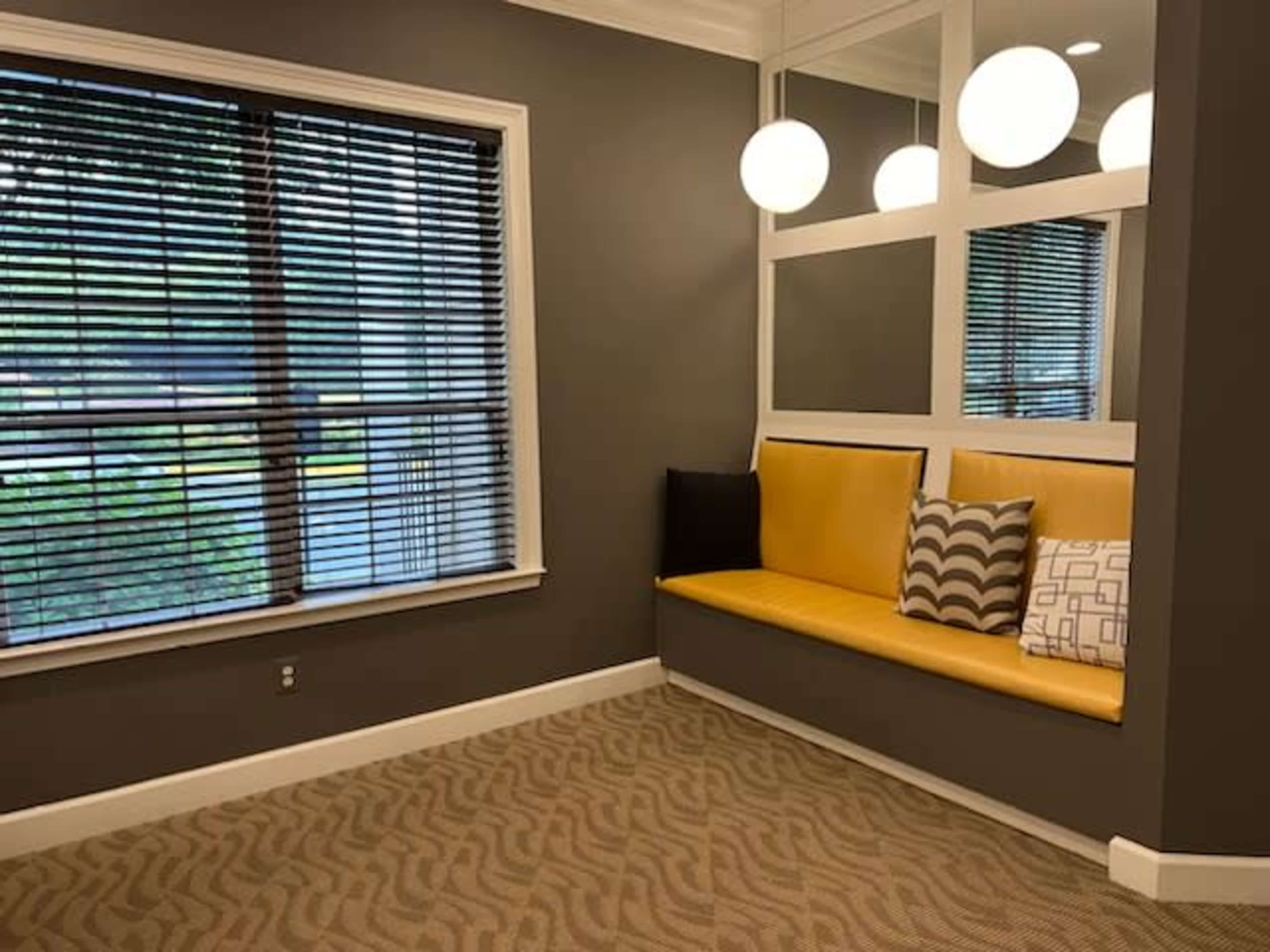 A modern waiting area with a yellow cushioned bench, gray walls, and large window with horizontal blinds.