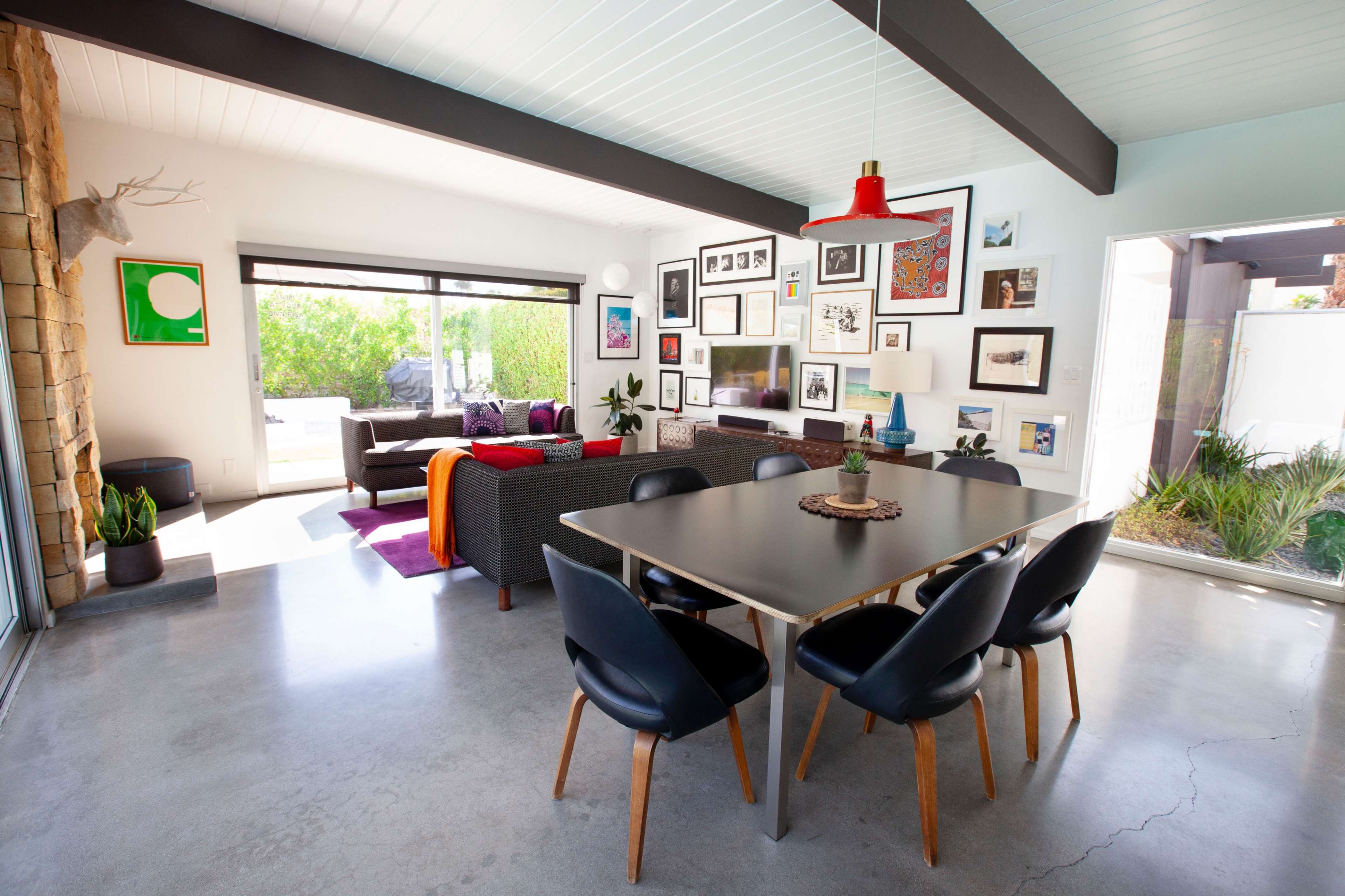 The image depicts a modern interior space featuring a dining area with a table and chairs, a living area with a couch, and walls adorned with framed artwork.