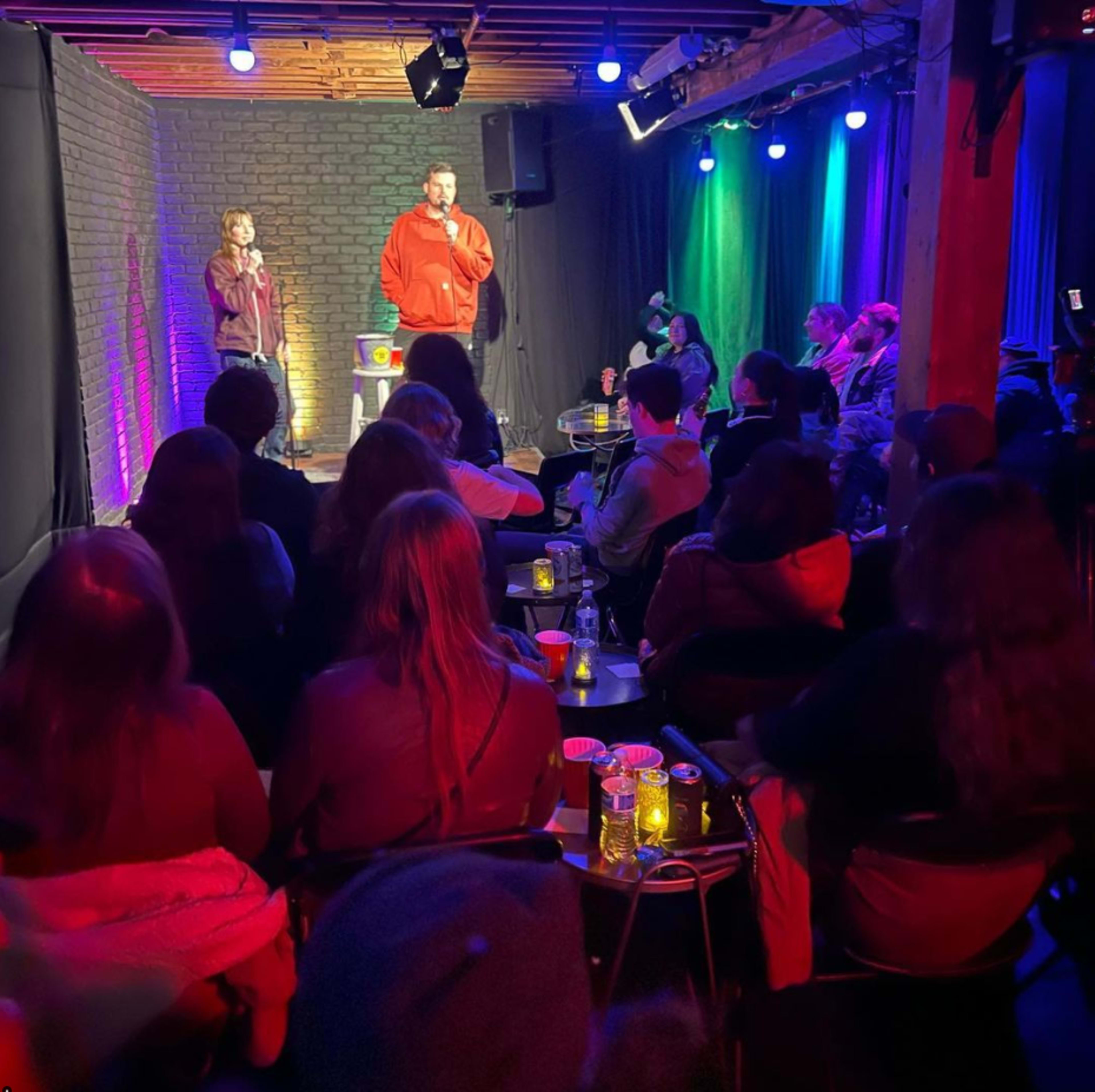 A comedian performs on stage in a cozy venue while an audience watches attentively from their seats.