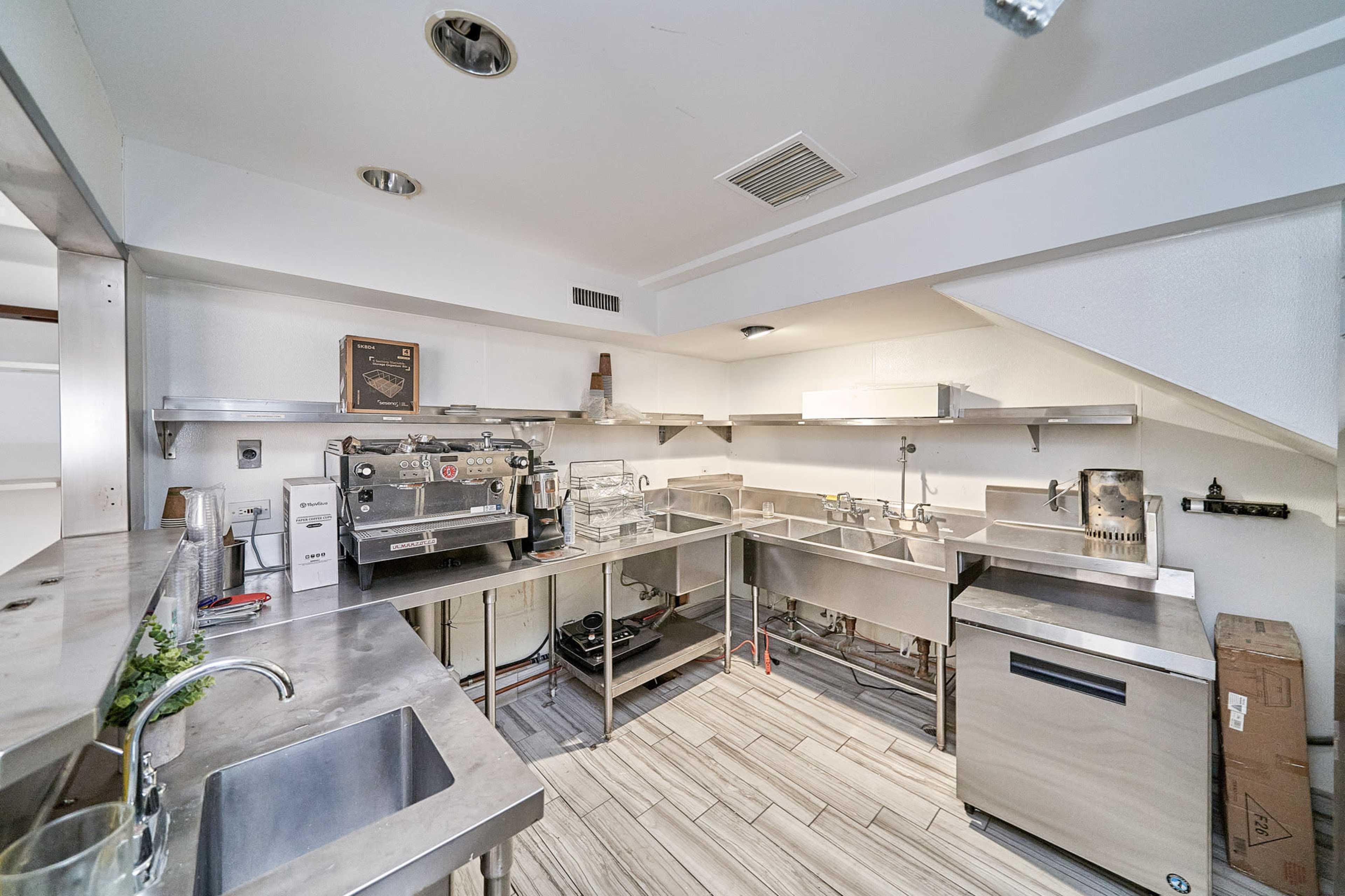 A clean, stainless steel kitchen with various appliances and workstations, including an espresso machine and sinks.