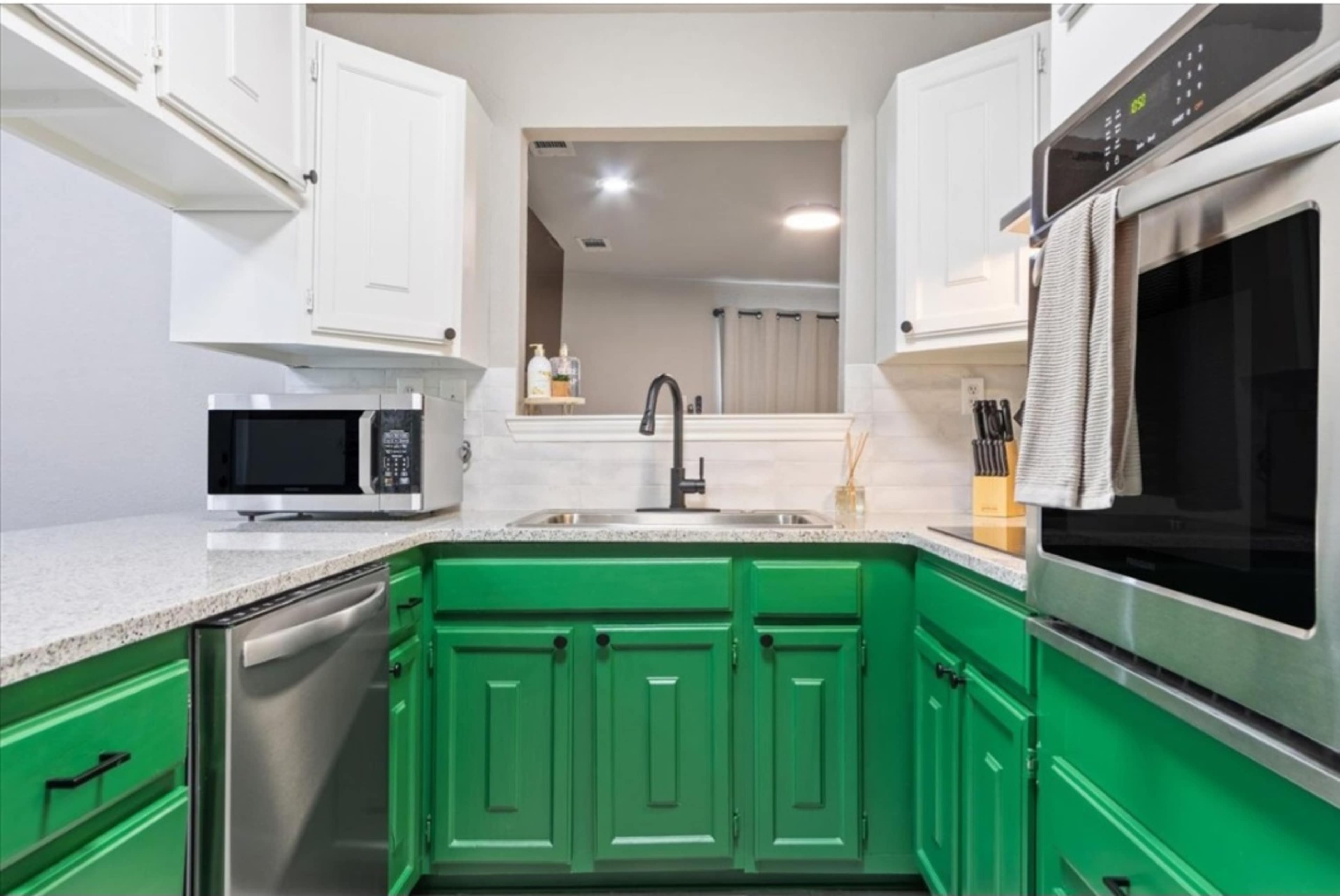 A kitchen with green lower cabinets, white upper cabinets, stainless steel appliances, and a dual-basin sink.