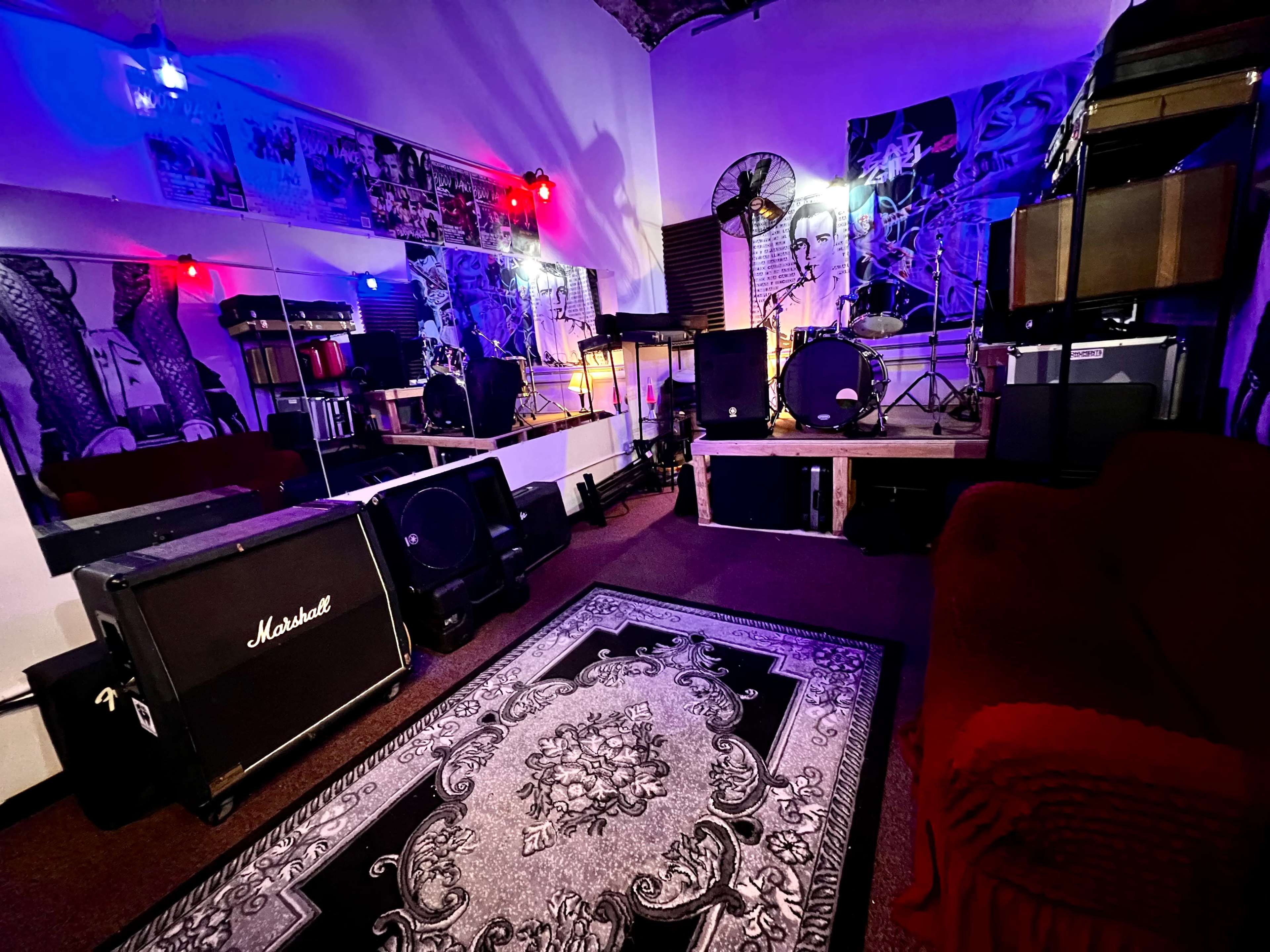 The image shows a music practice room with amplifiers, drums, and colorful stage lights reflected in mirrors.
