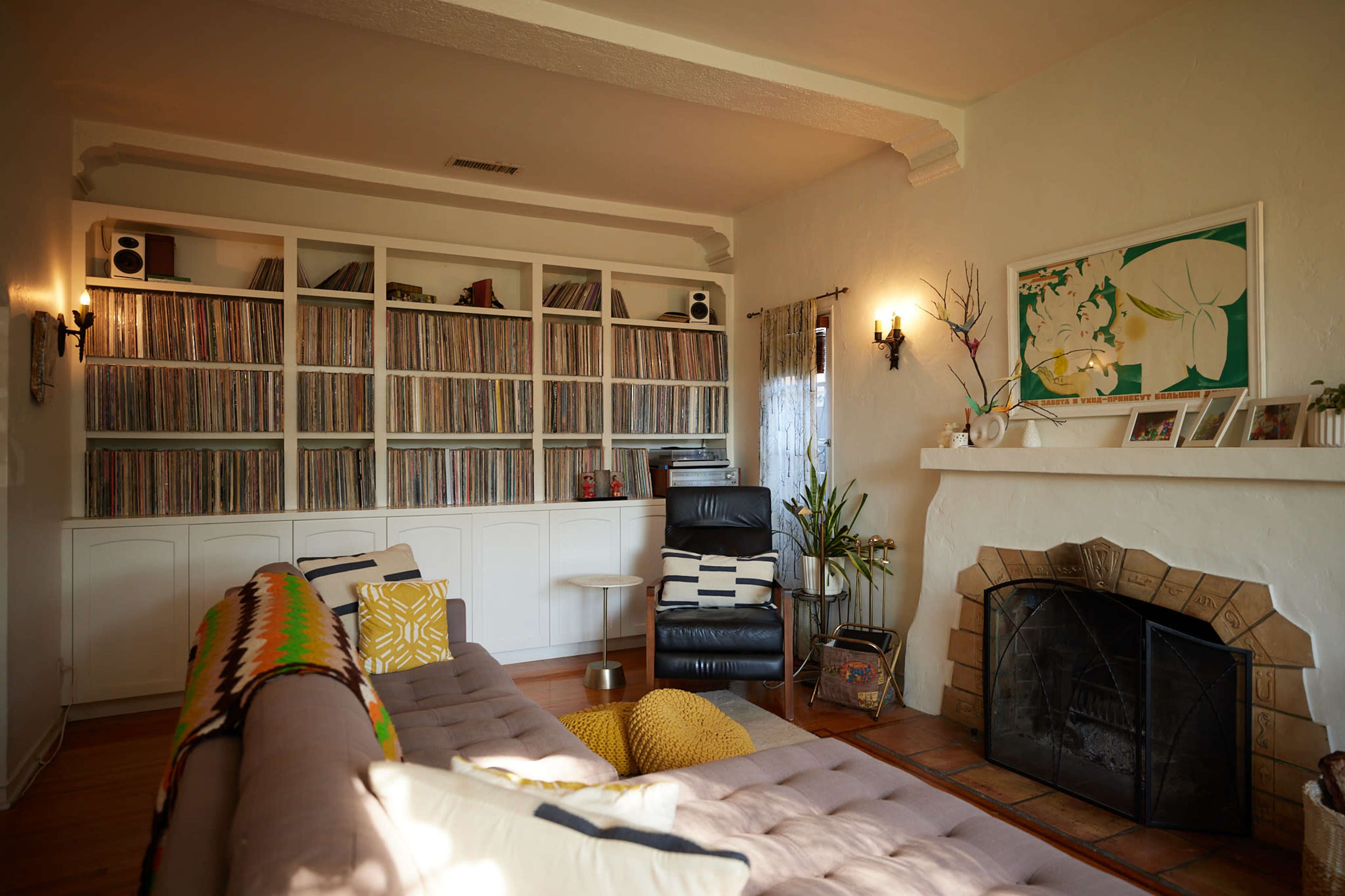 A living room features a large bookshelf filled with vinyl records, a comfortable couch, a black recliner, and a fireplace with a decorative mantel.