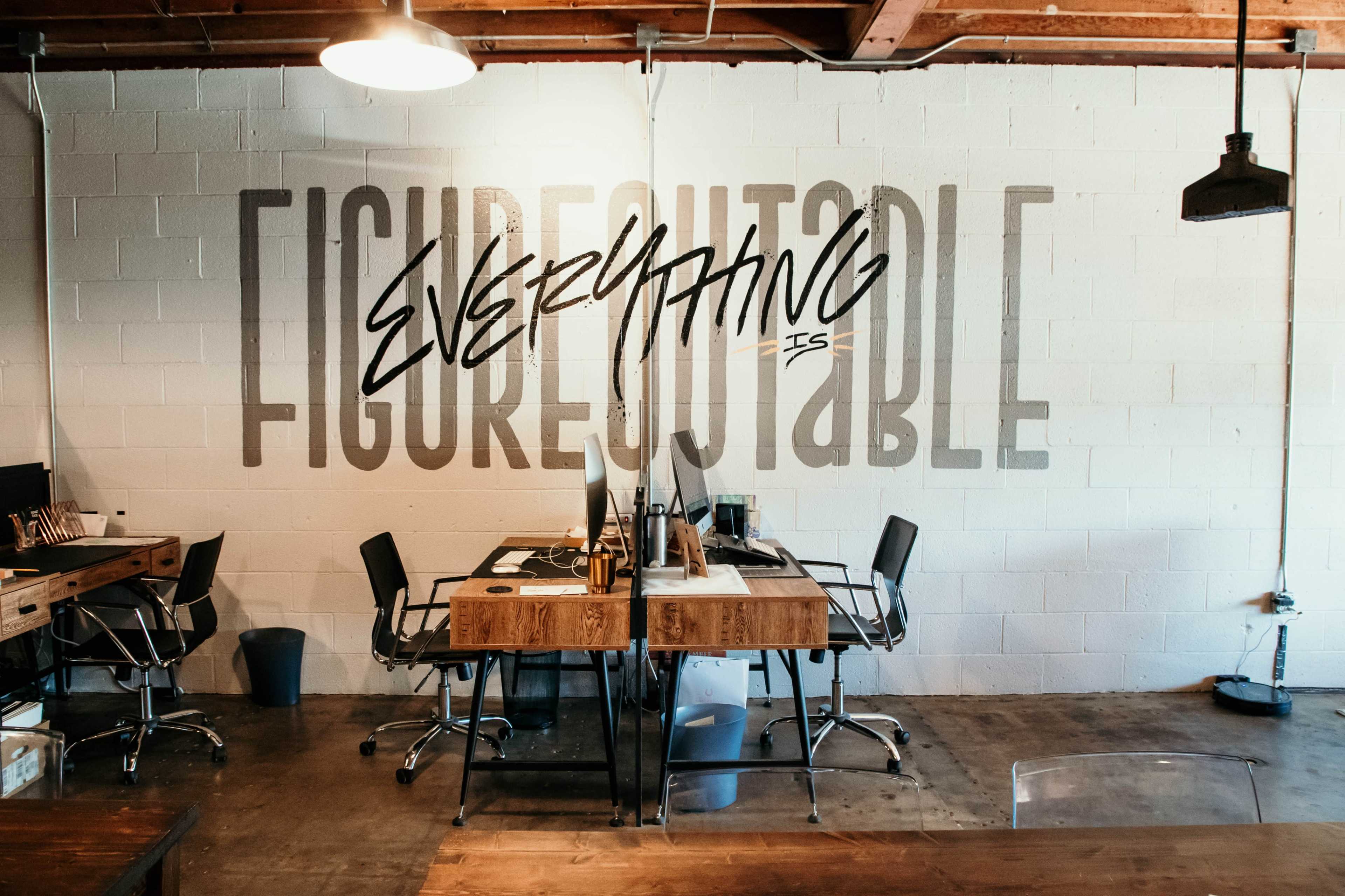 An office space with wooden desks, chairs, and a large wall featuring the phrase "EVERYTHING IS FIGURABLE" in bold lettering.