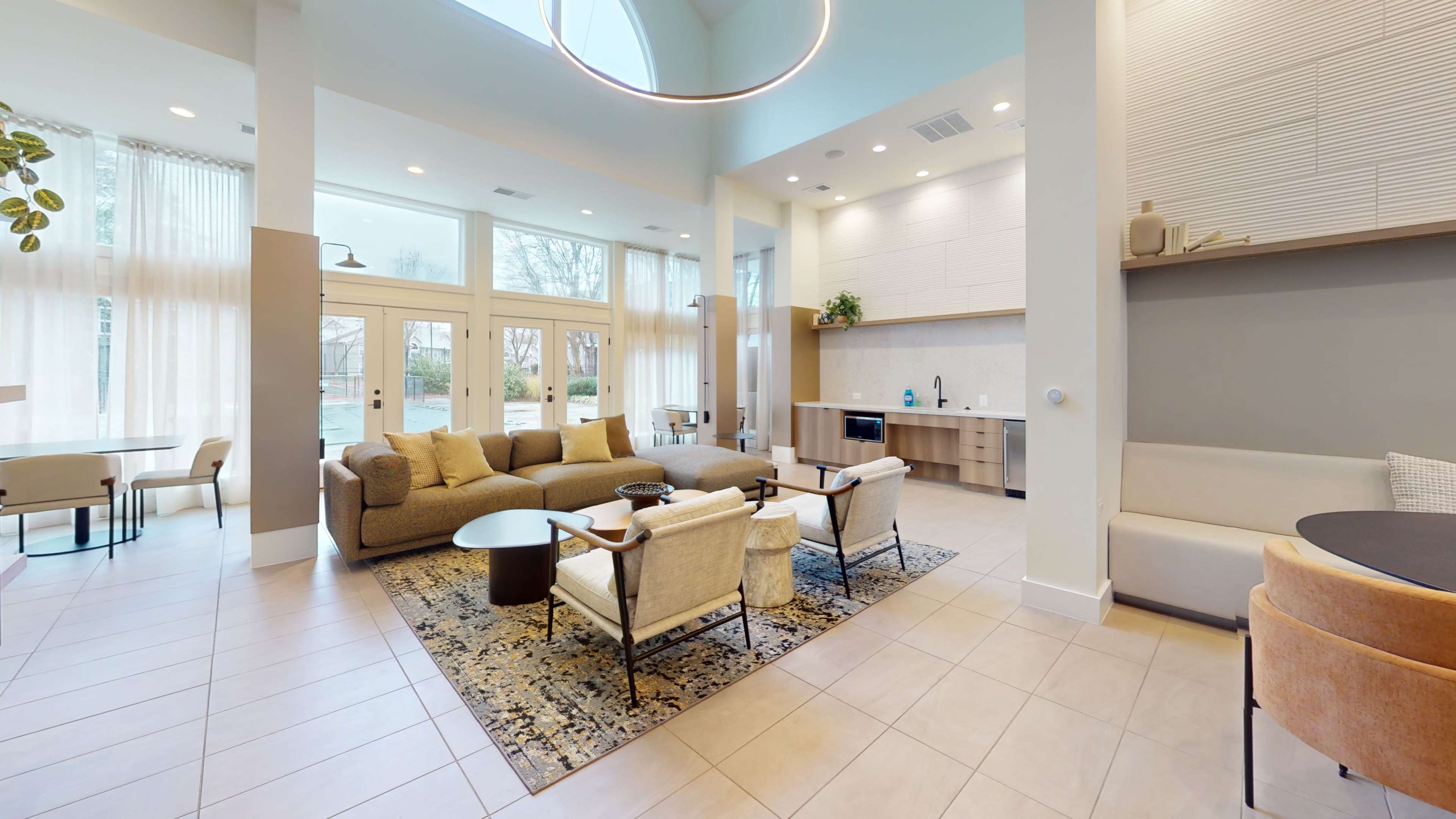 A modern lounge area with a light-colored sofa, armchairs, a round coffee table, and large windows allowing natural light to fill the space.