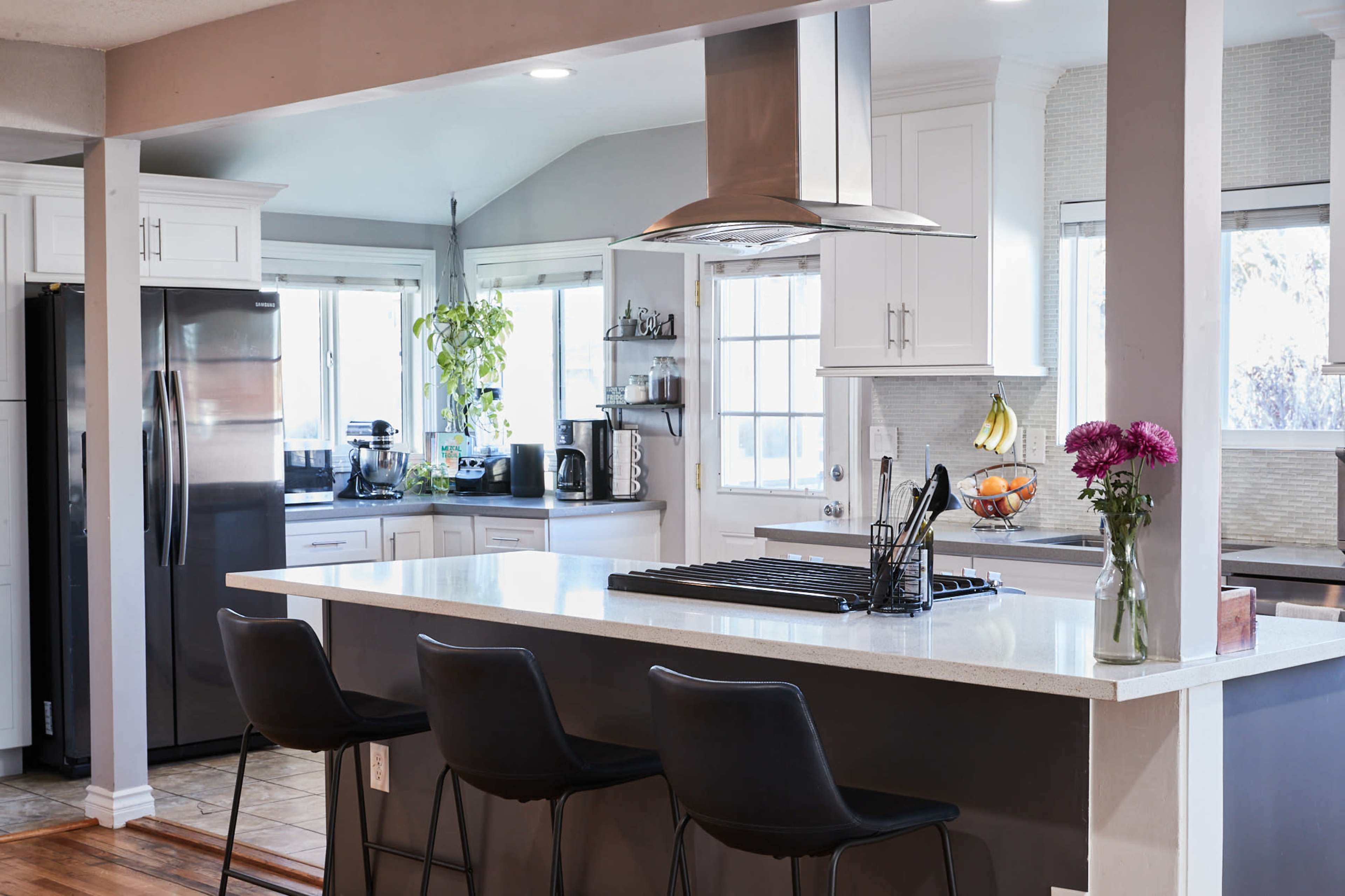 The image shows a modern kitchen with white cabinets, a large island with bar stools, and stainless steel appliances.