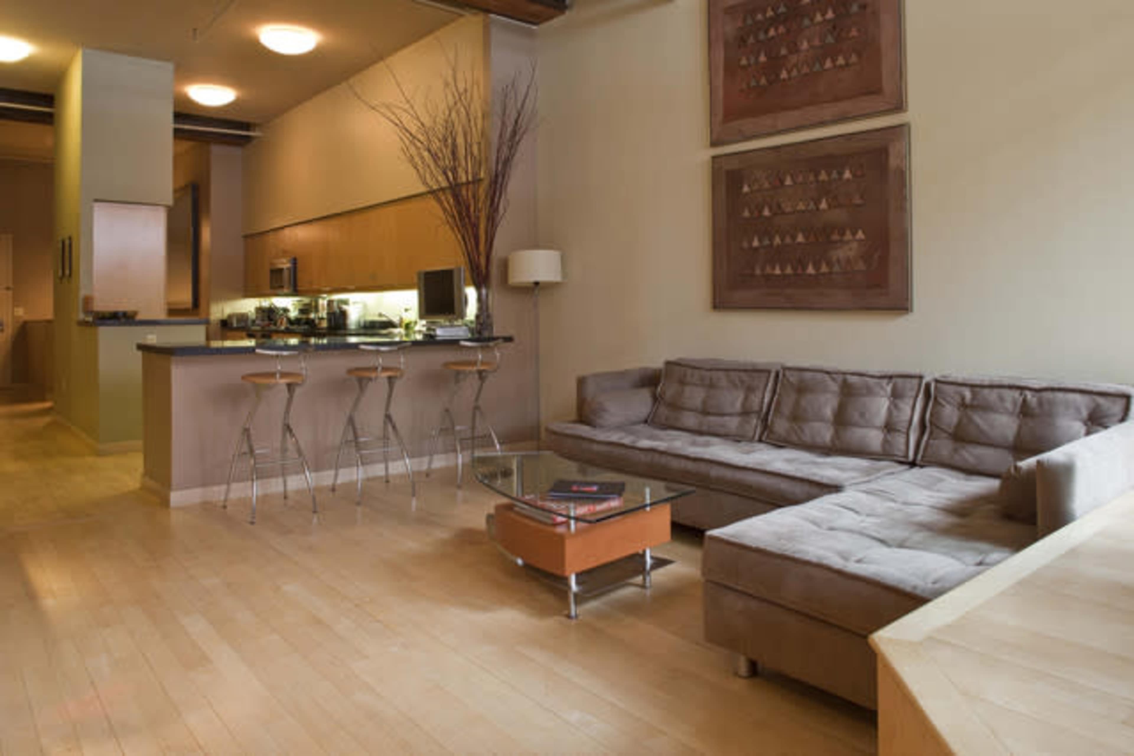 A modern living room with a sectional sofa, a glass coffee table, and a kitchen area in the background.
