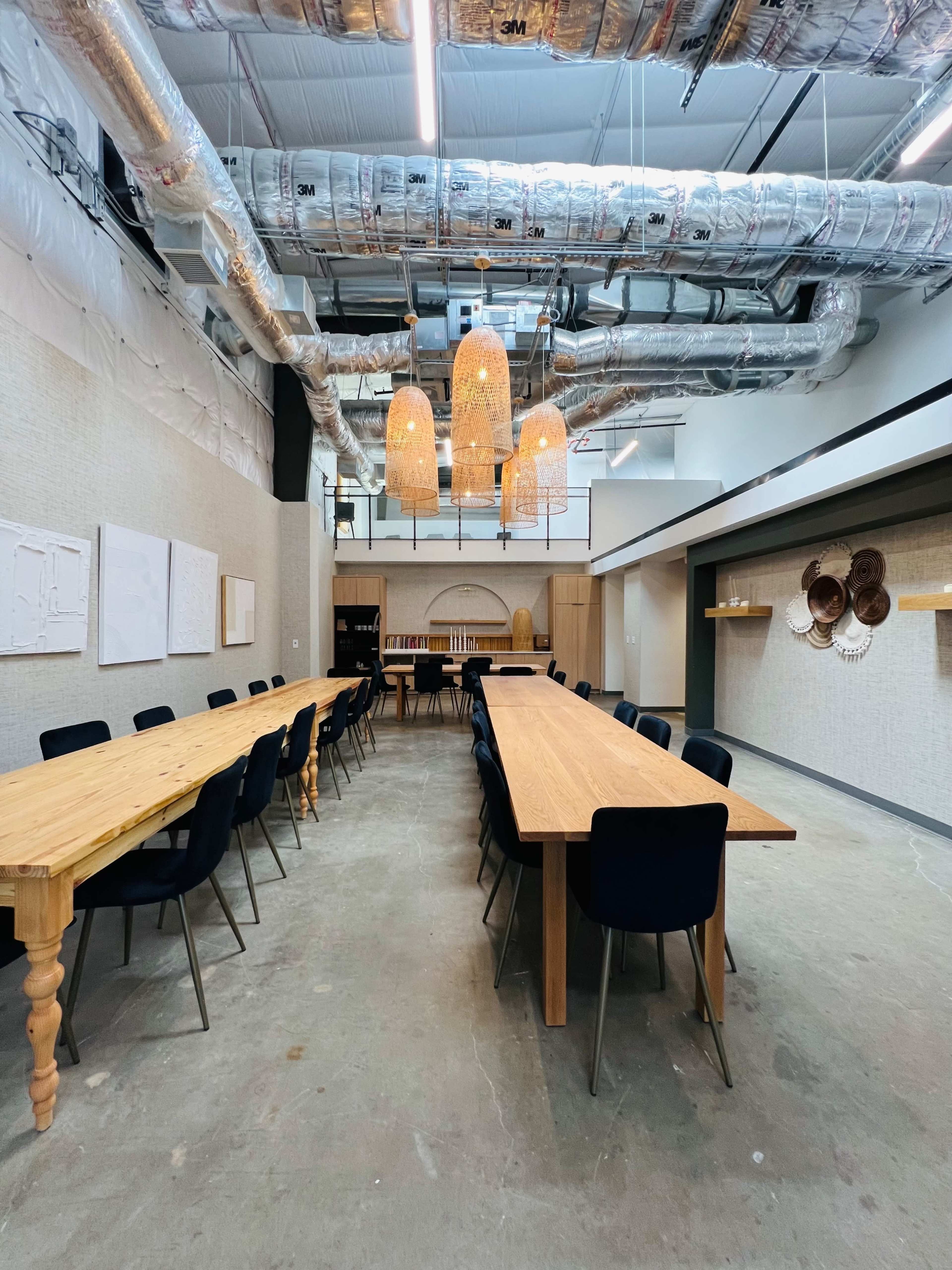 A long, narrow meeting room with wooden tables, black chairs, and several pendant lights hanging from the ceiling.