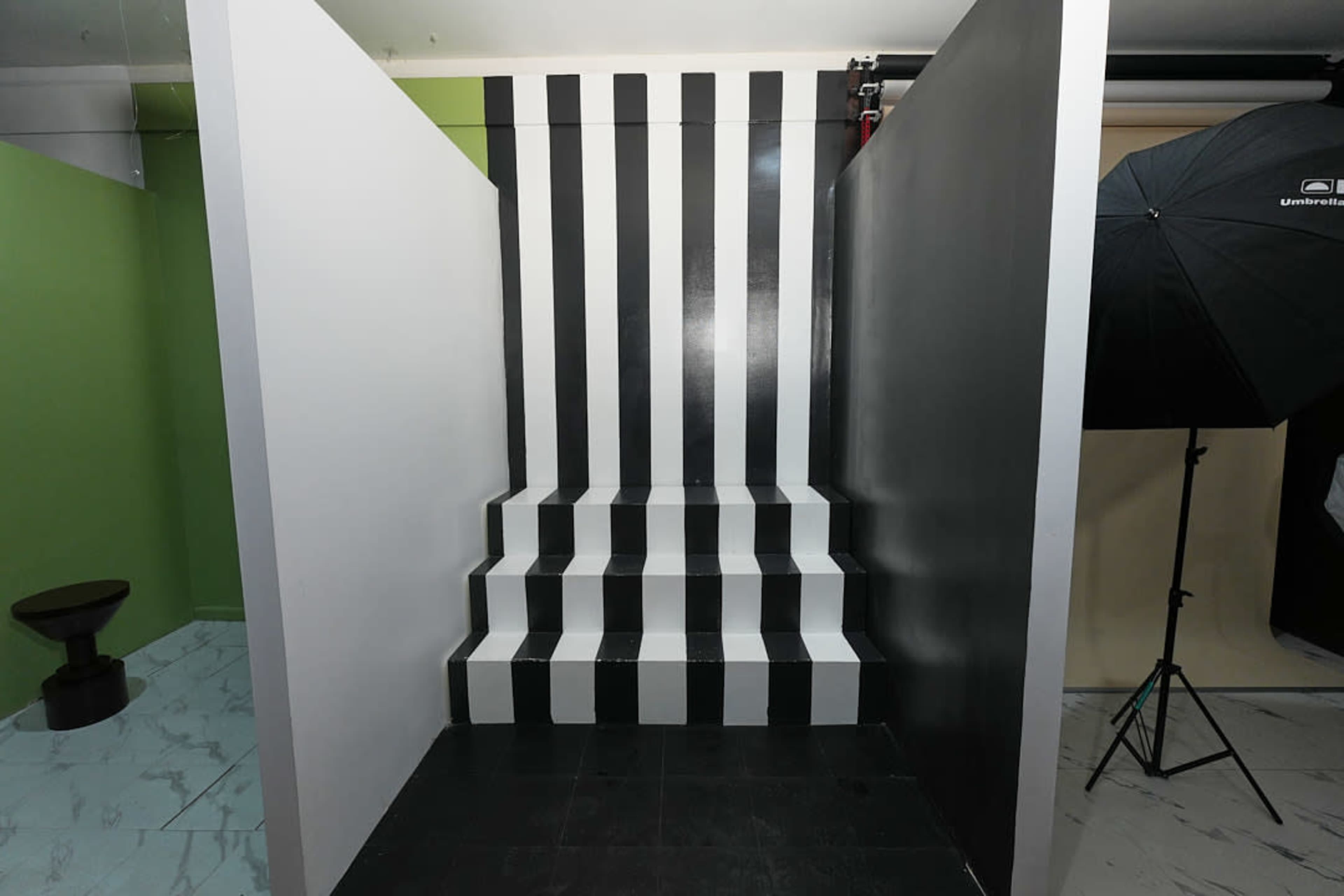 The image shows a staircase painted with alternating black and white stripes, framed by two plain walls, one in green and the other in black.