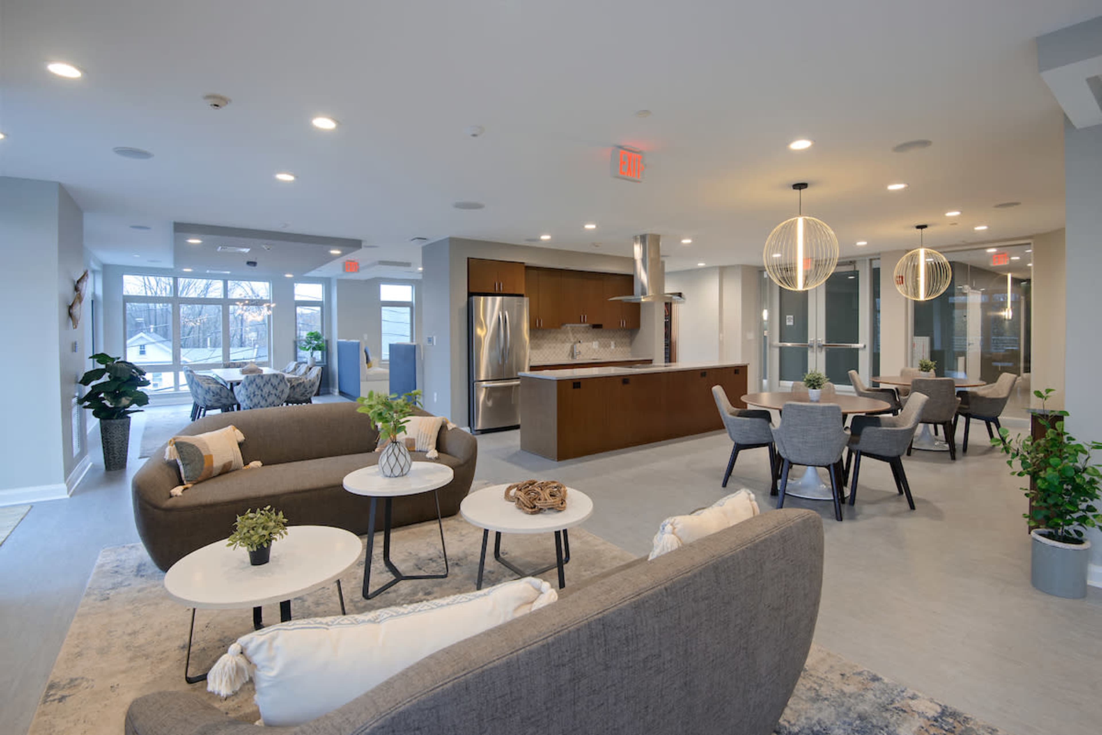 A modern common area with sofas, tables, kitchen appliances, and dining seating arrangement, illuminated by pendant lights.