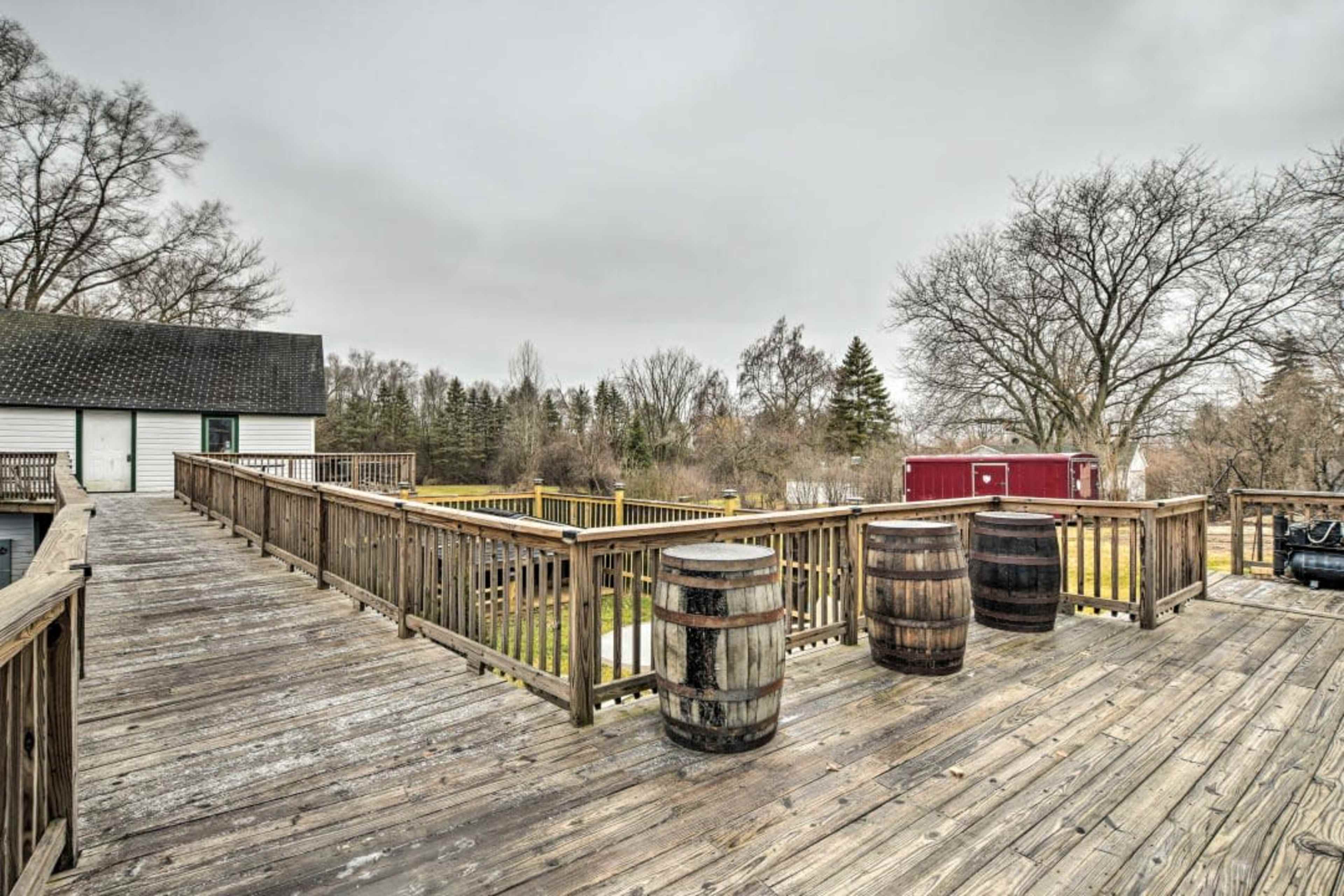 A wooden deck with three barrels placed on it, surrounded by trees and distant buildings under a cloudy sky.