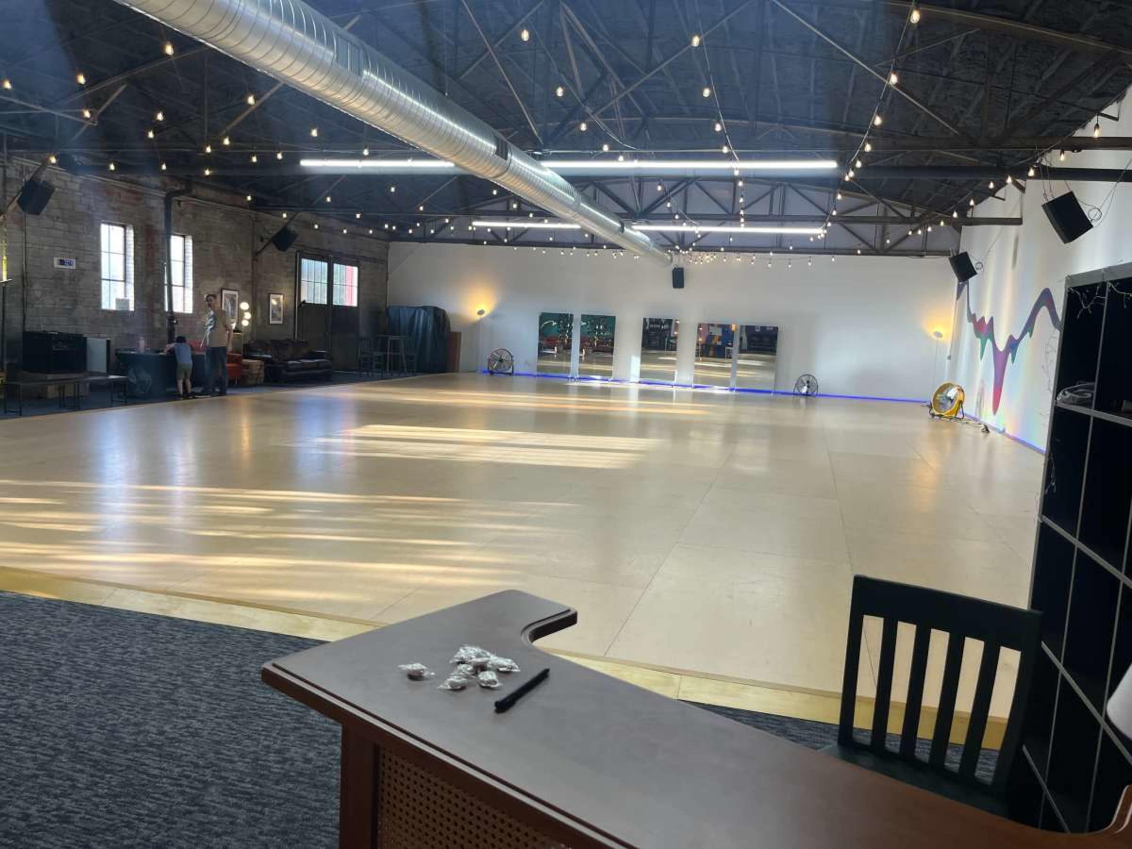 A spacious dance studio with wooden flooring, large mirrors, and industrial-style lighting.