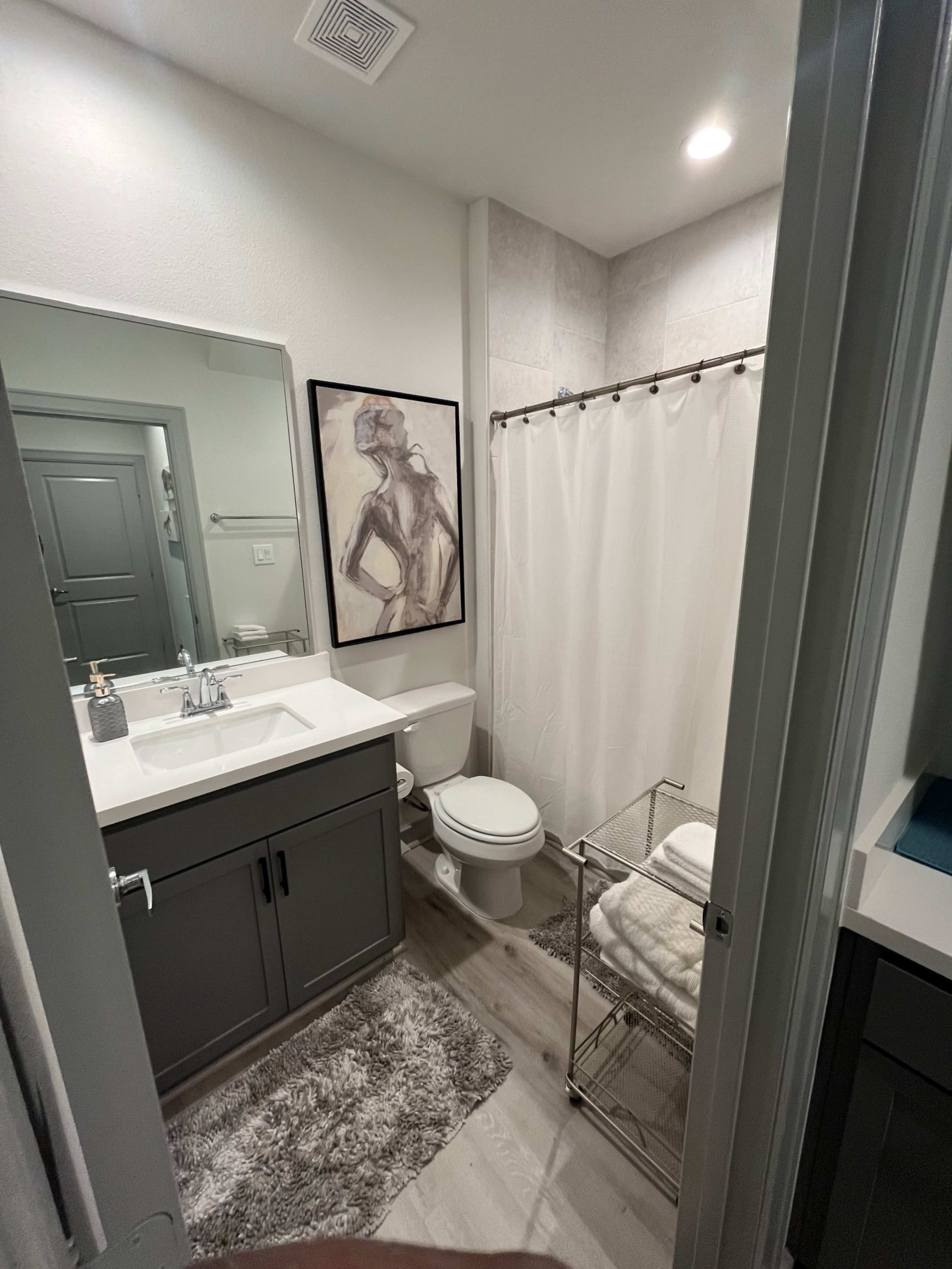 A small bathroom featuring a vanity with a sink, a toilet, a shower with a curtain, and a towel rack with neatly stacked towels.