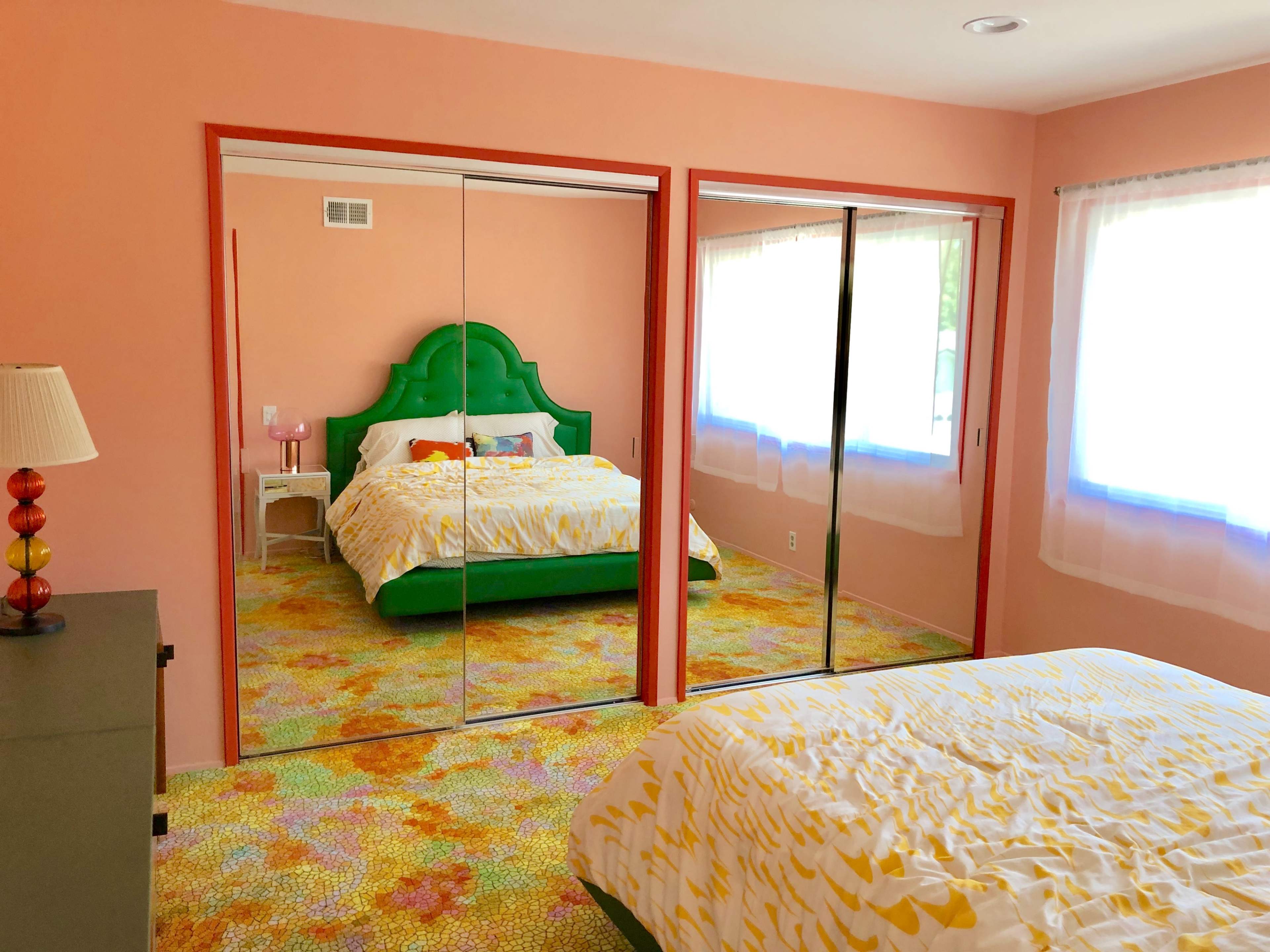 A brightly colored bedroom featuring a green headboard, a bed with a yellow and white comforter, and mirrored closet doors reflecting the room's decor.