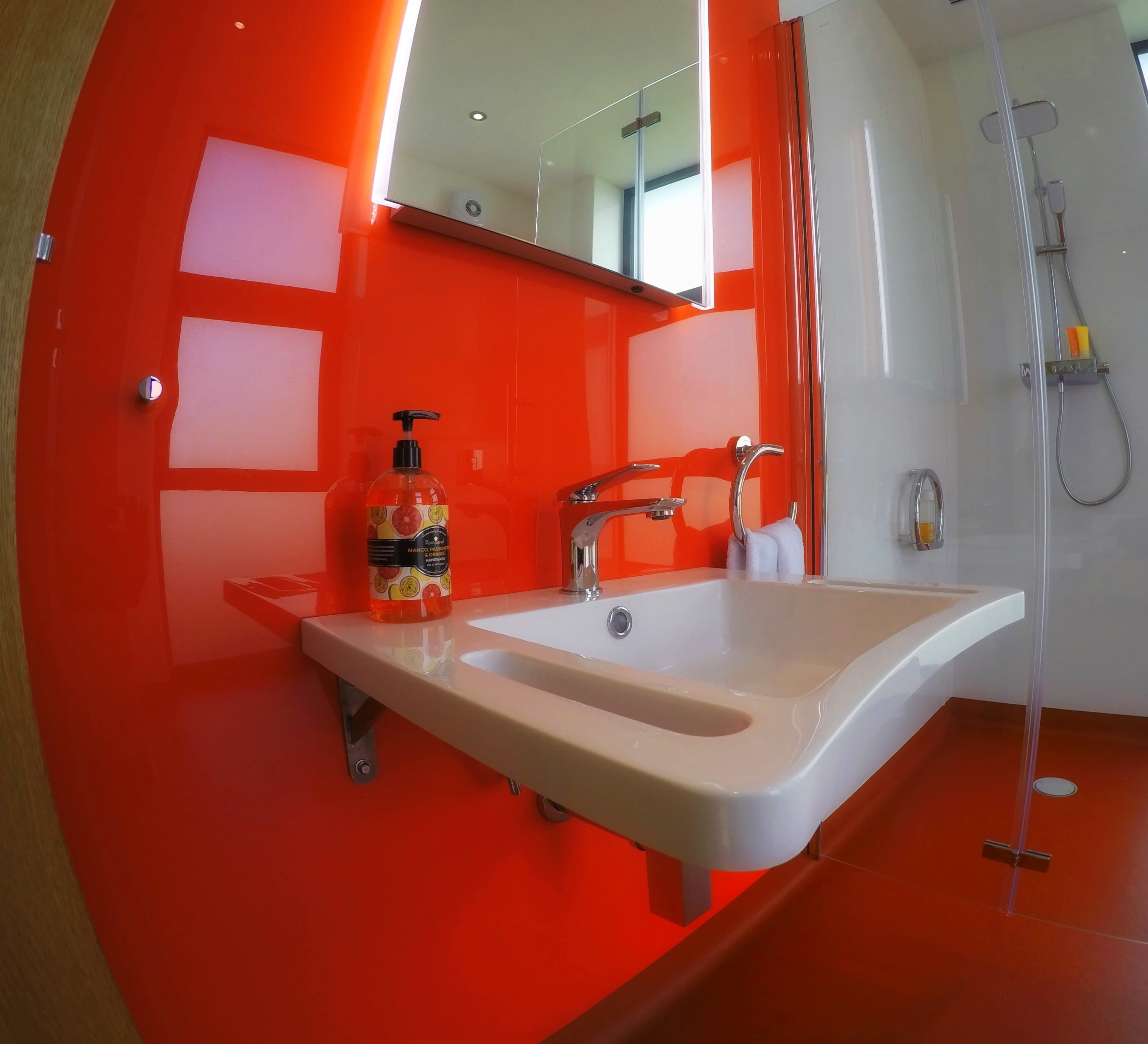 A modern bathroom featuring a bright red wall, a white sink with a faucet, and a mirror above the sink.