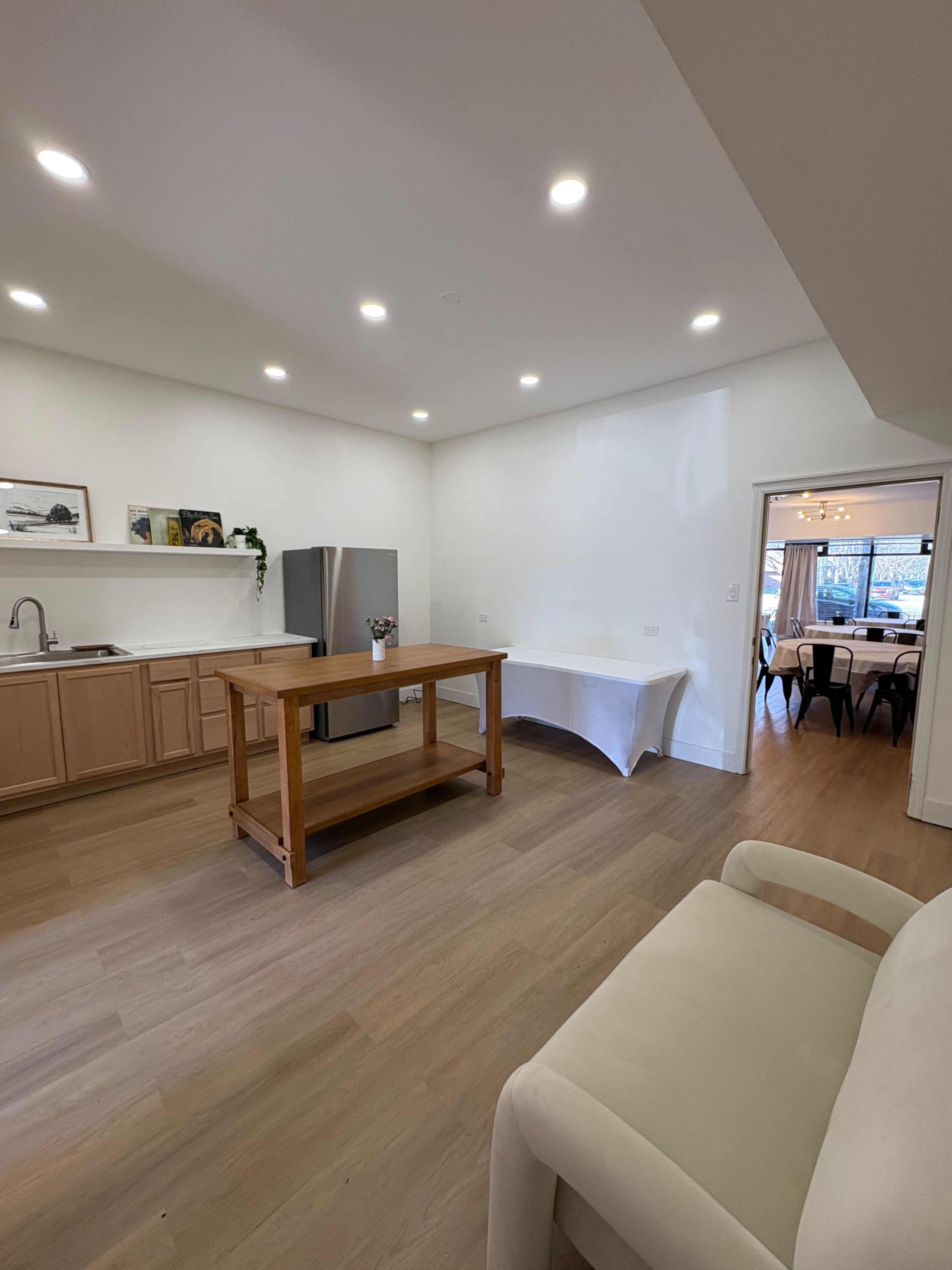 The image shows a modern kitchen featuring light wood cabinetry, a stainless steel refrigerator, and a central wooden island.