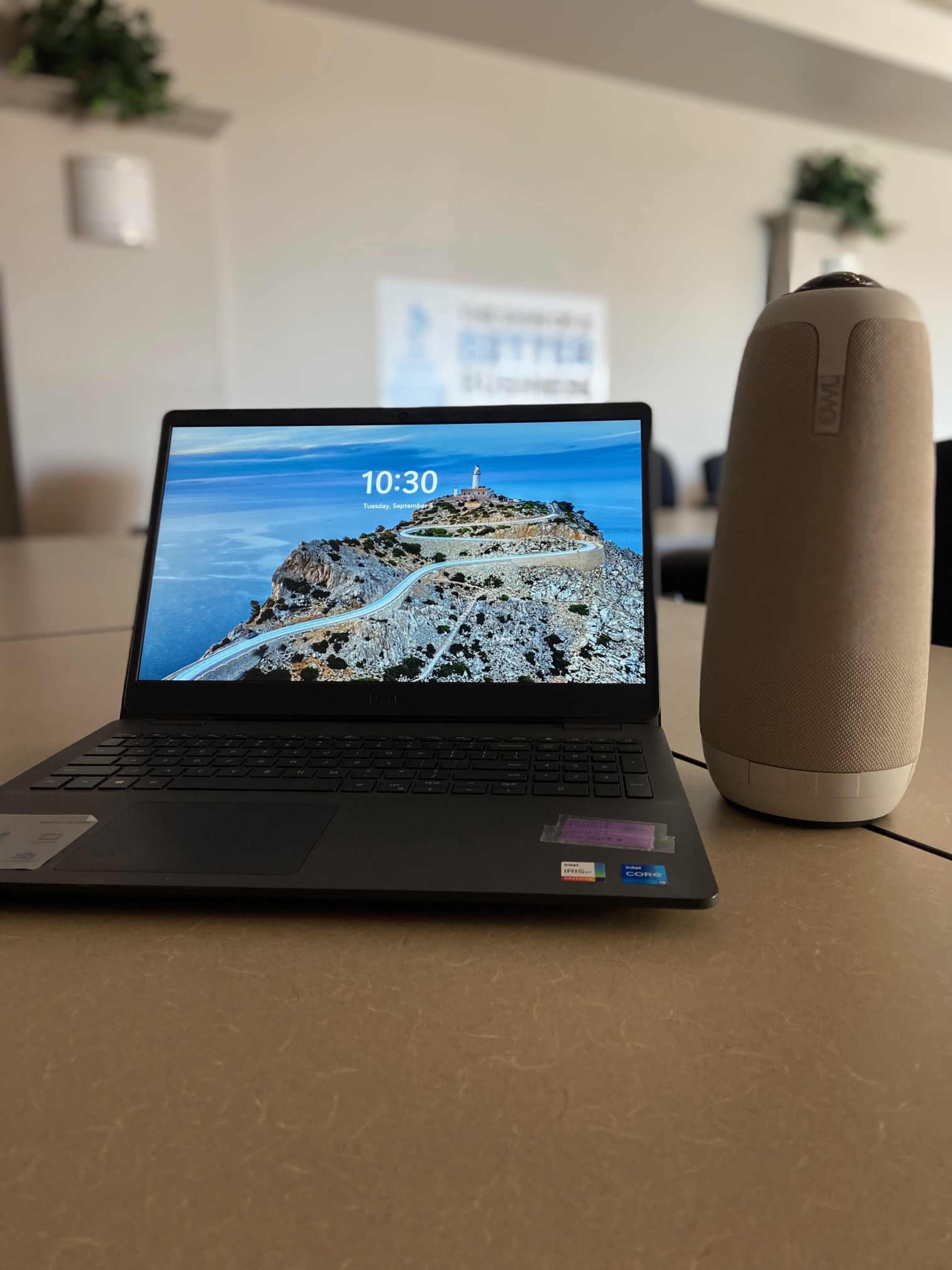A laptop displaying a scenic coastal image sits next to a cylindrical speaker on a table.