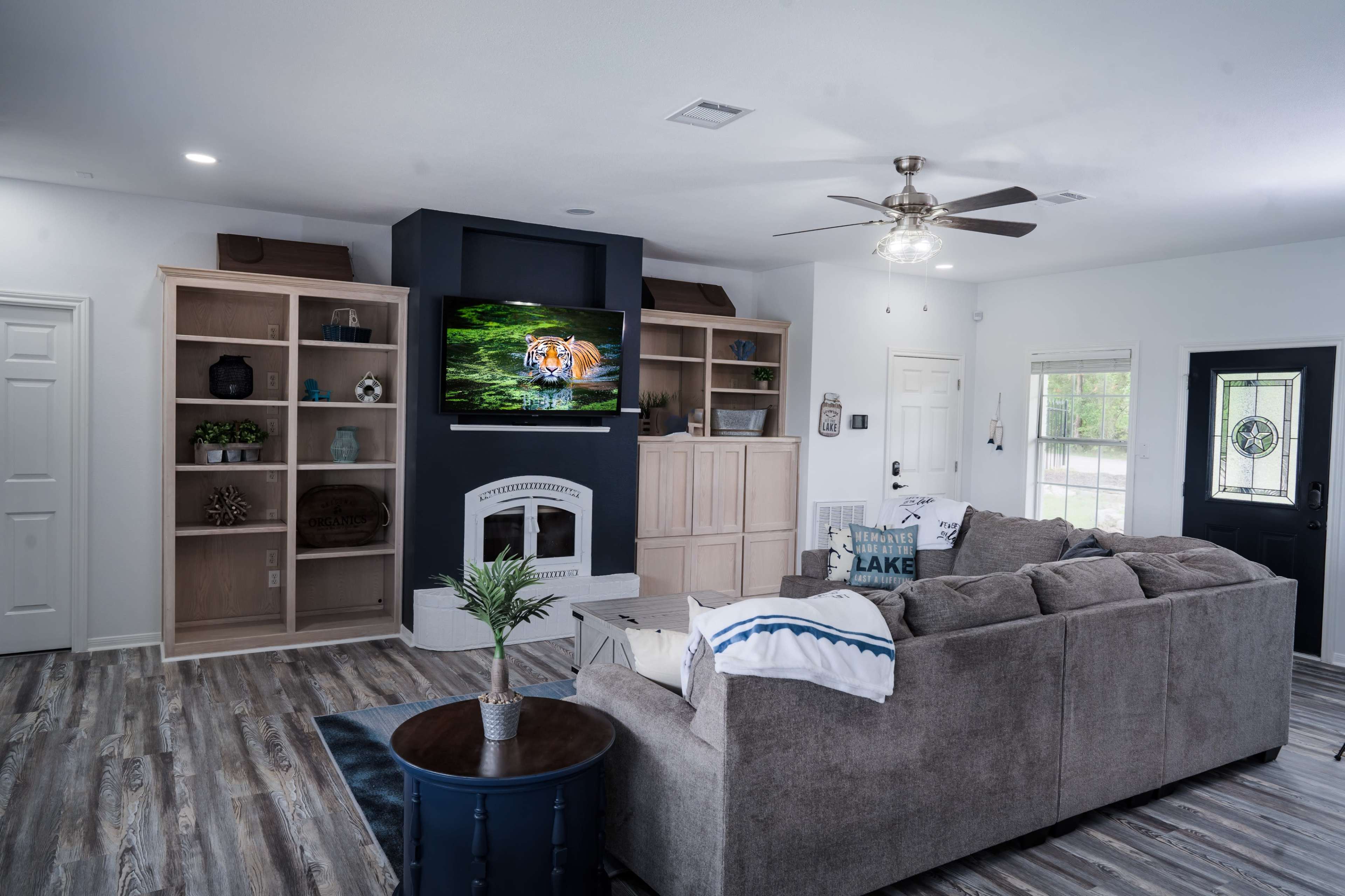 A spacious living room features a large sectional sofa, a mounted television, built-in shelving, and a front door with a decorative window.