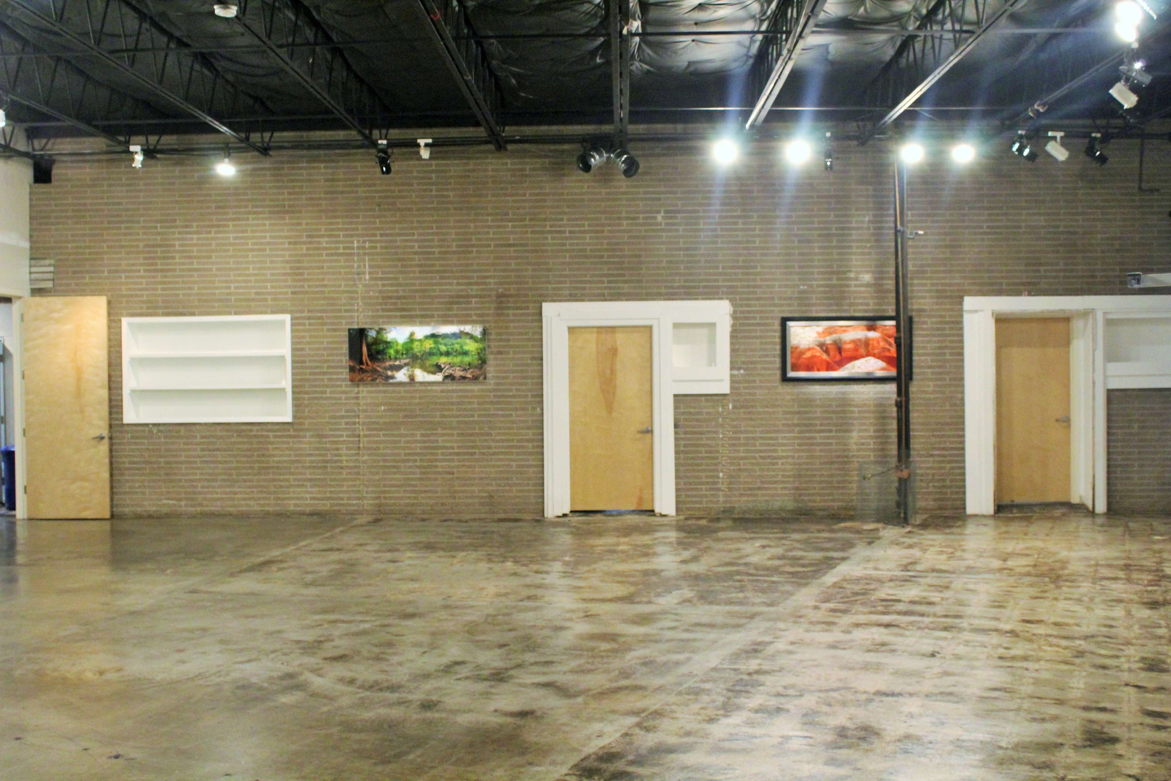 A spacious, empty interior with brick walls, two doors, and framed photographs hanging on the wall.